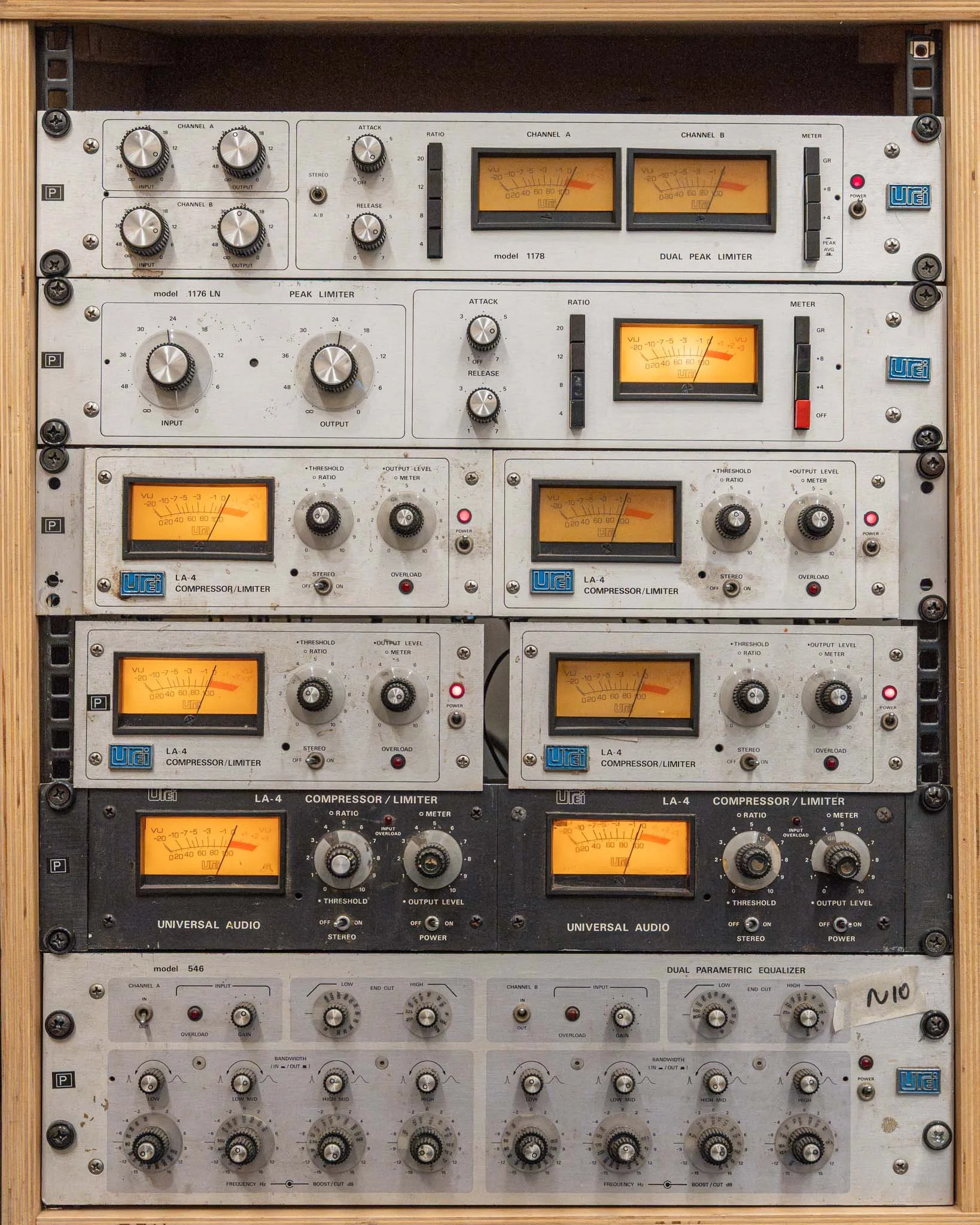 Stacked audio equipment including compressors, limiters, and equalizers, with meters and knobs for volume and settings.