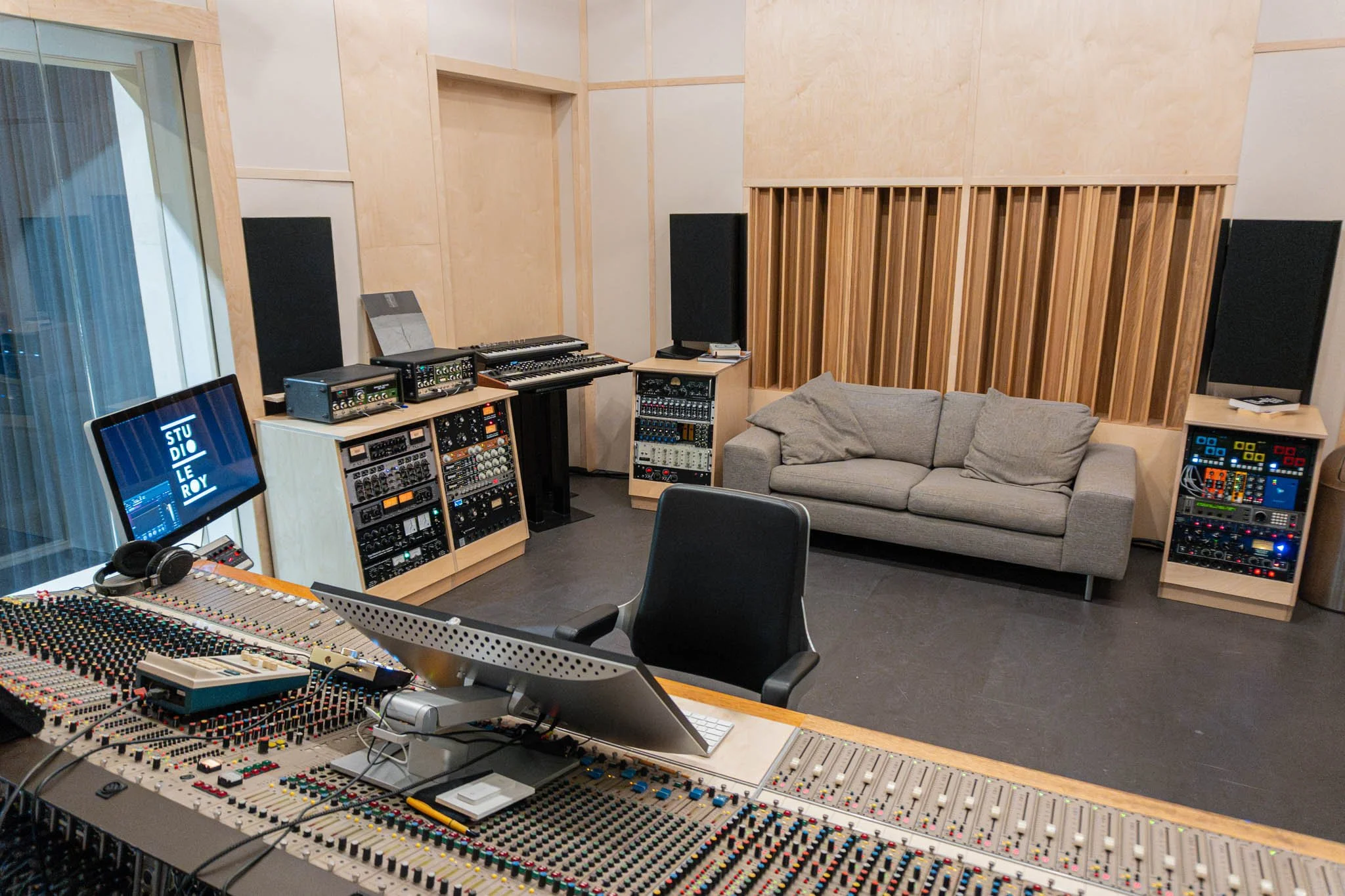 Recording studio with mixing console, computer monitor, sofa, sound equipment, and acoustic panels.