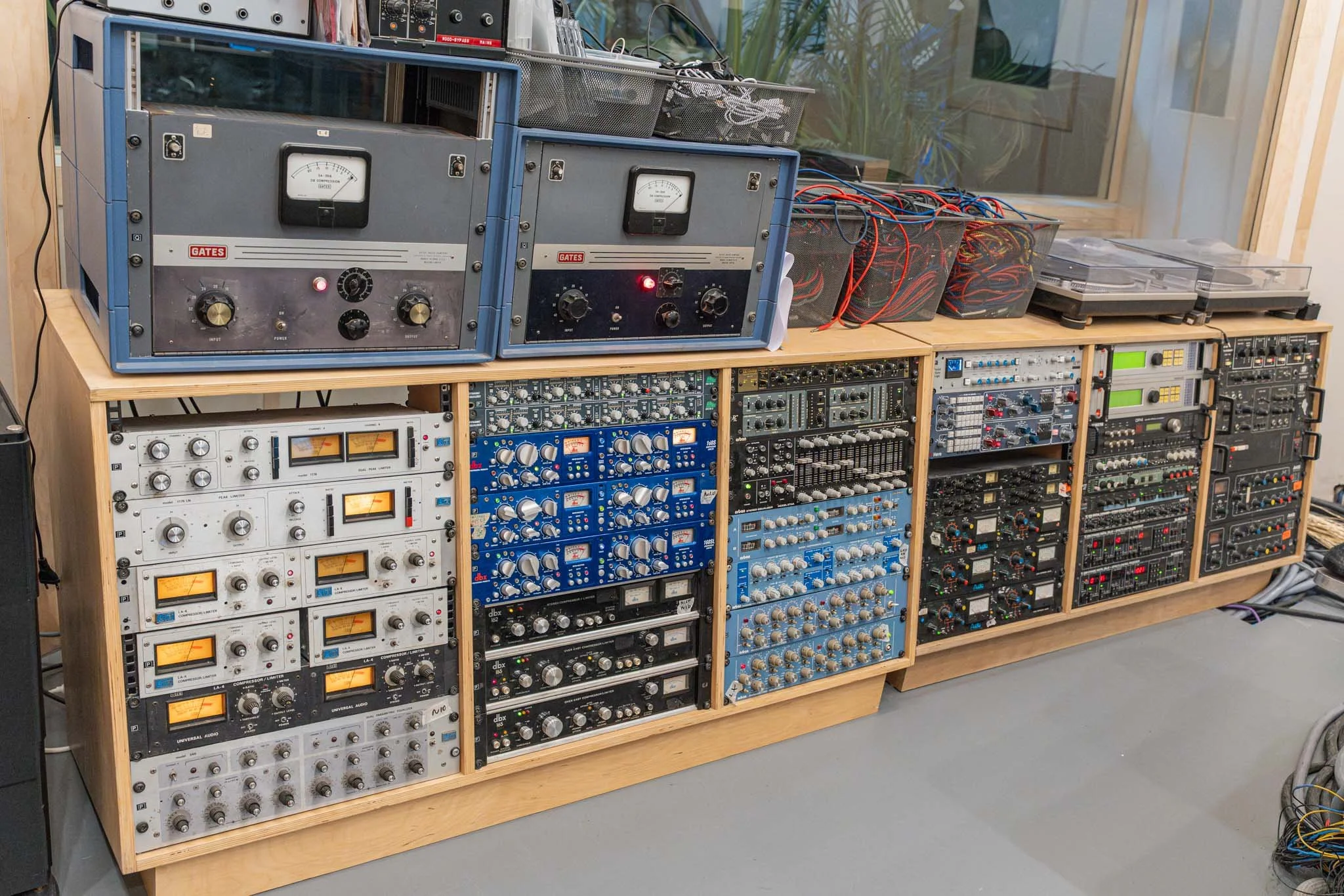Audio equipment and vintage electronics organized on a wooden shelving unit in a recording studio, including amplifiers, equalizers, and turntables.