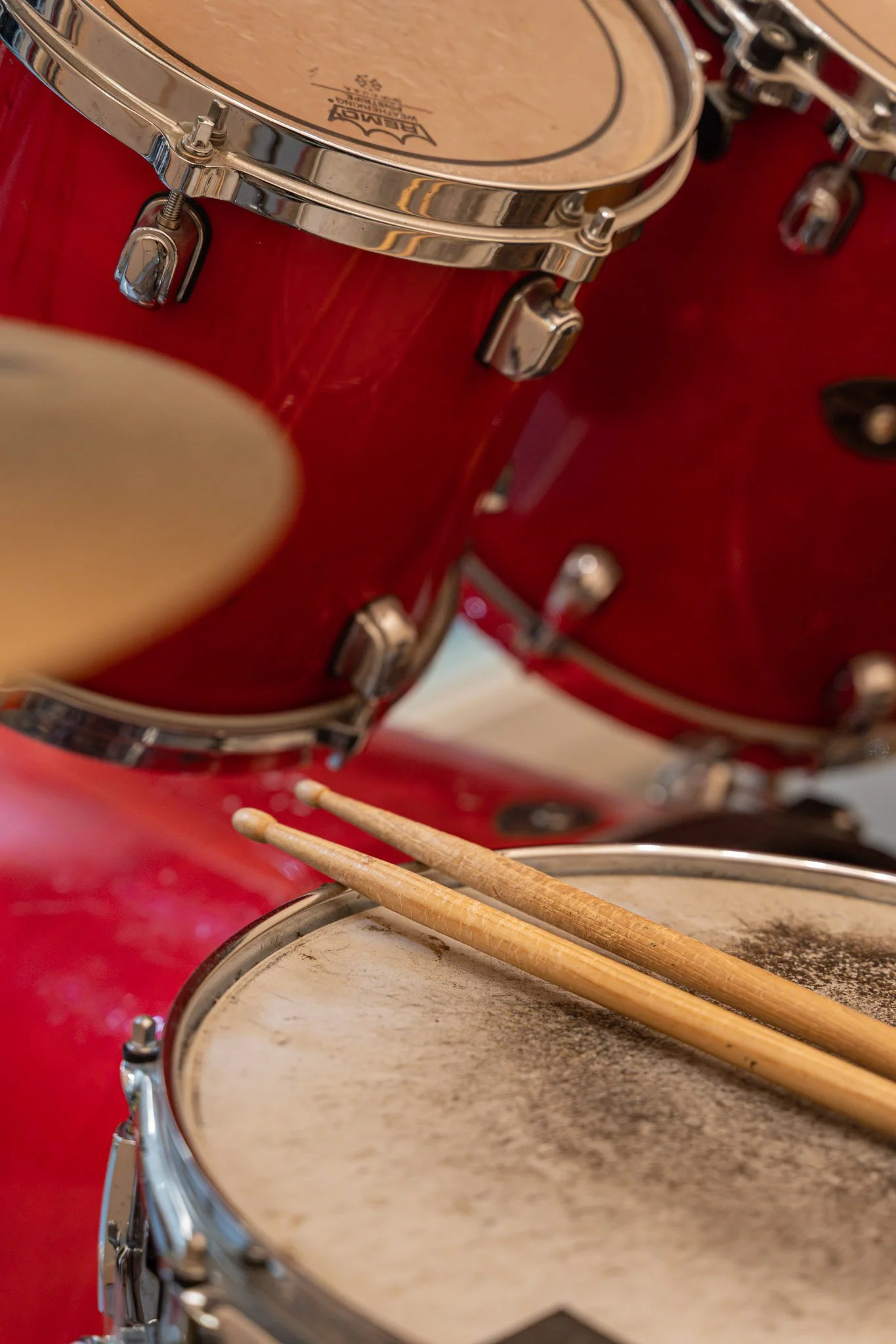 Close-up of a red drum set with two drumsticks resting on the snare drum, showing detailed hardware and textured drum surfaces.
