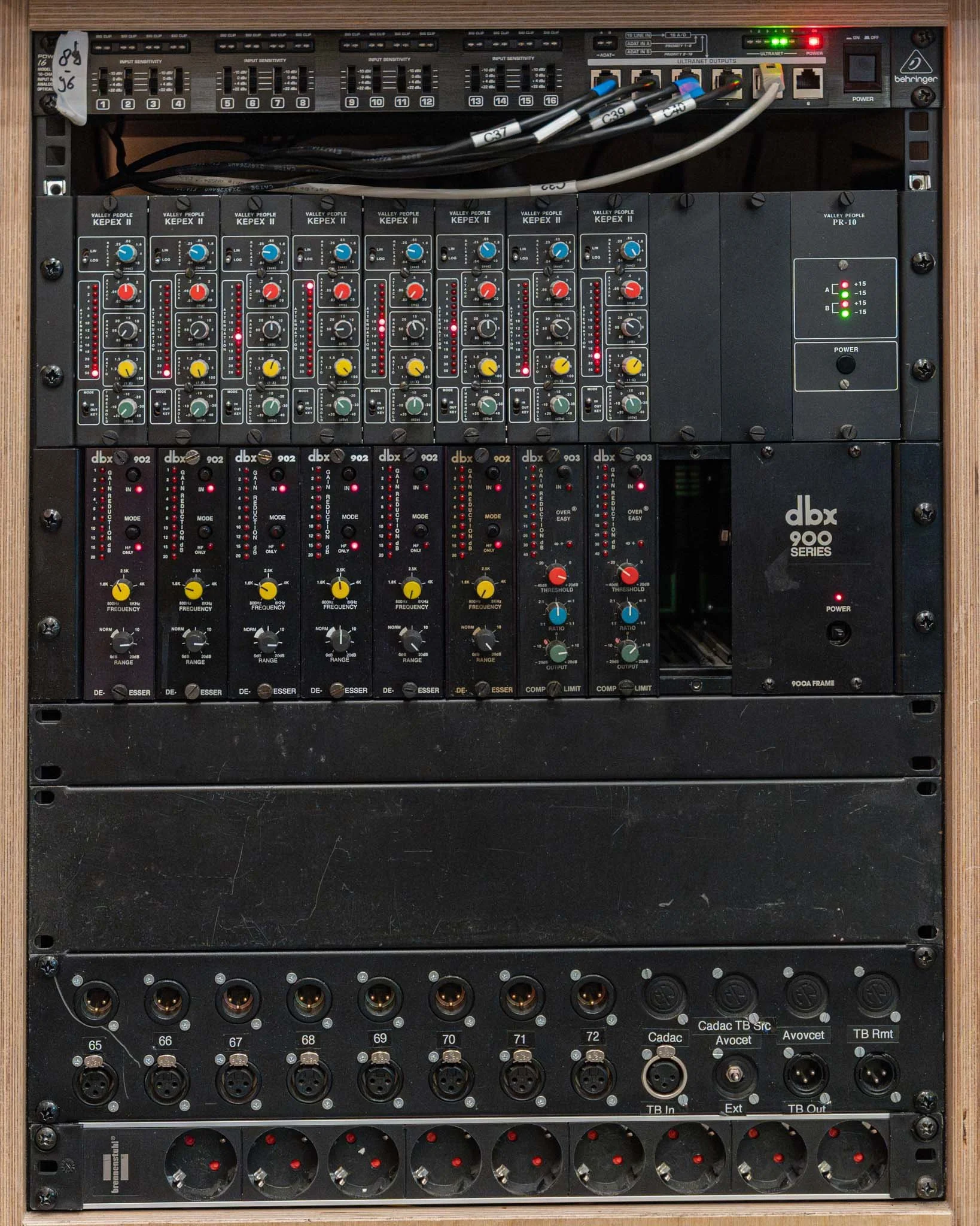 A rack-mounted audio equipment setup featuring a Behringer ULTRAGRAPH PRO, multiple KEPEX II and PR-10 audio processors, dbx 902 and 903 series EQs, and various audio connectors and inputs.