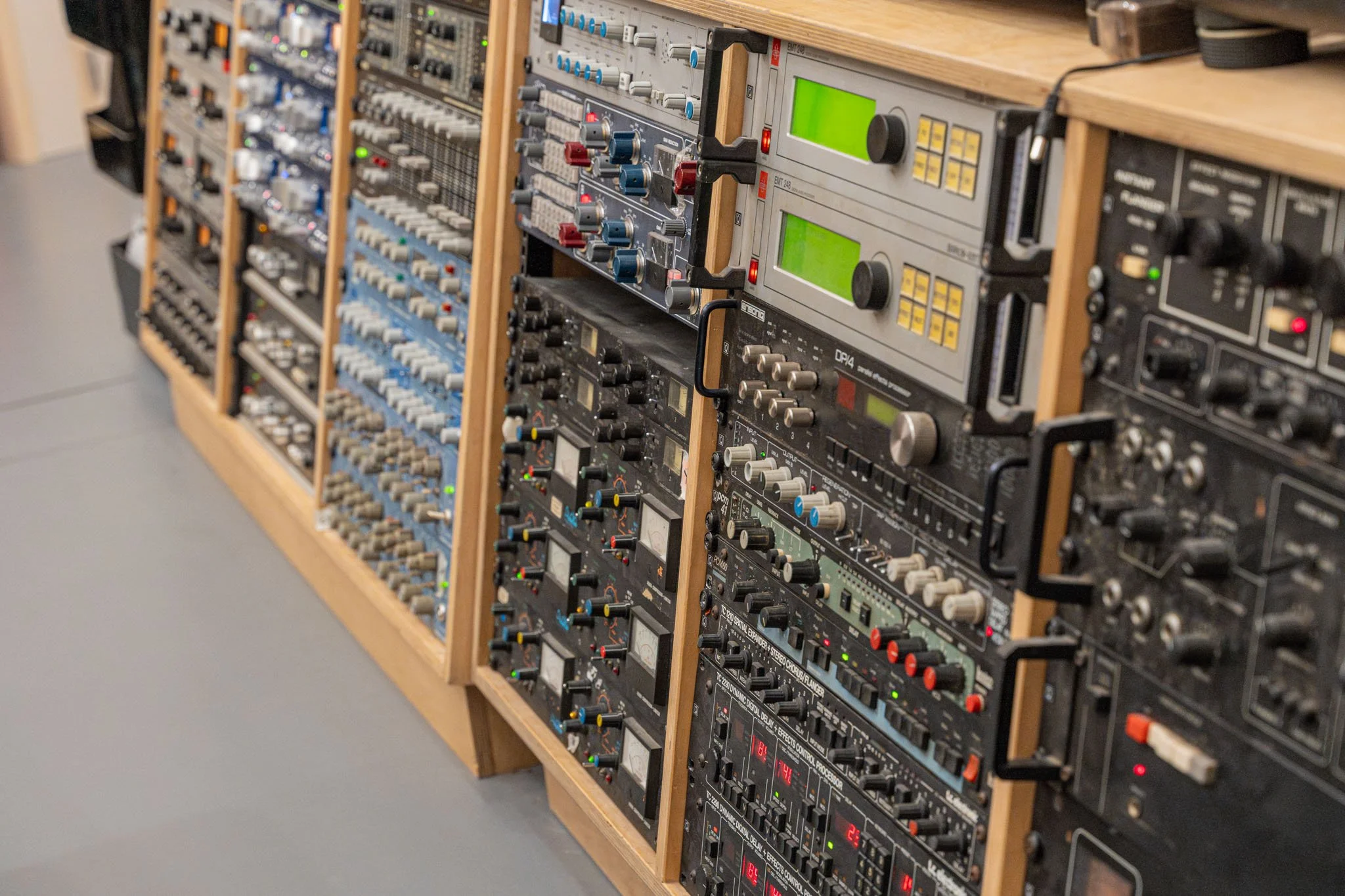 Rack of vintage audio and recording equipment with various knobs, buttons, and digital displays.