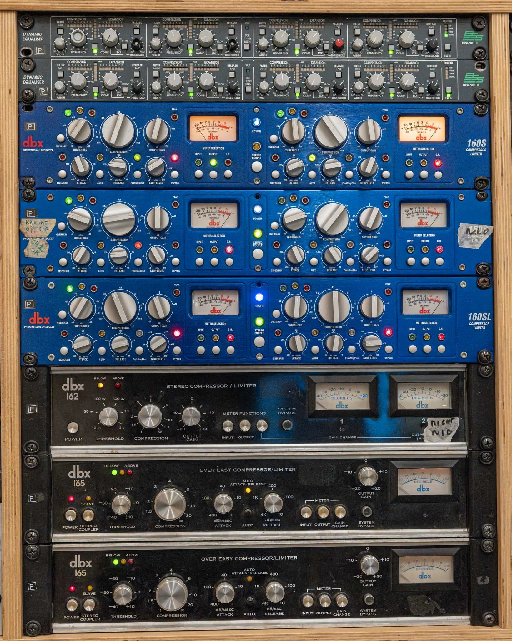 A large rack of professional audio equipment, including equalizers, compressors, limiters, and stereo compression/limiting units, all with various knobs, switches, and meters for controlling sound.