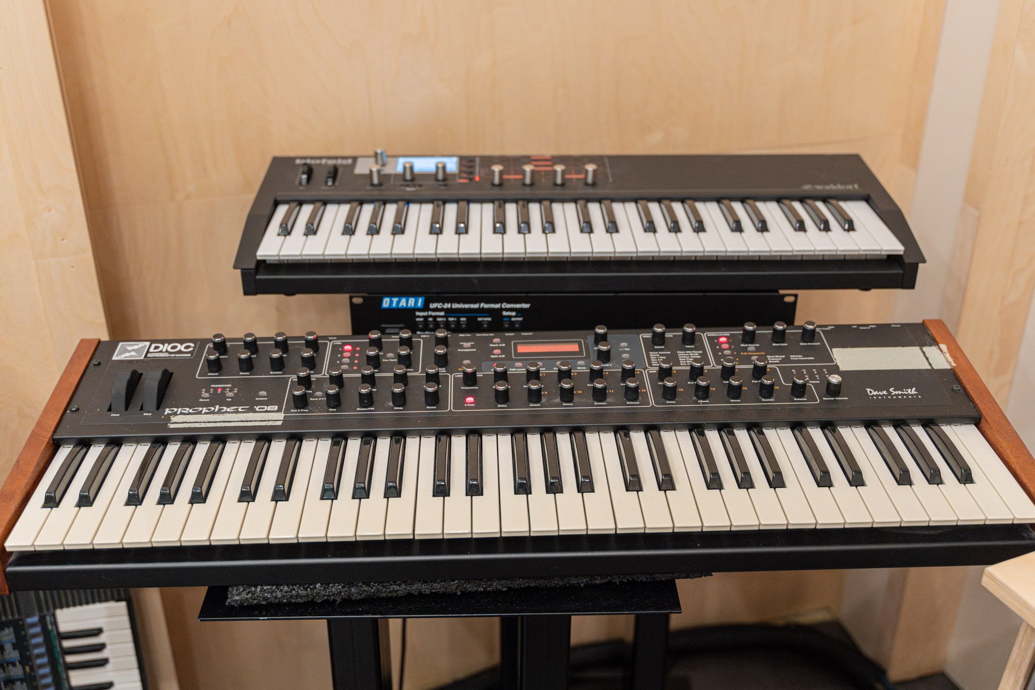 Two musical keyboards placed one above the other on a stand in a room with light-colored wooden walls.