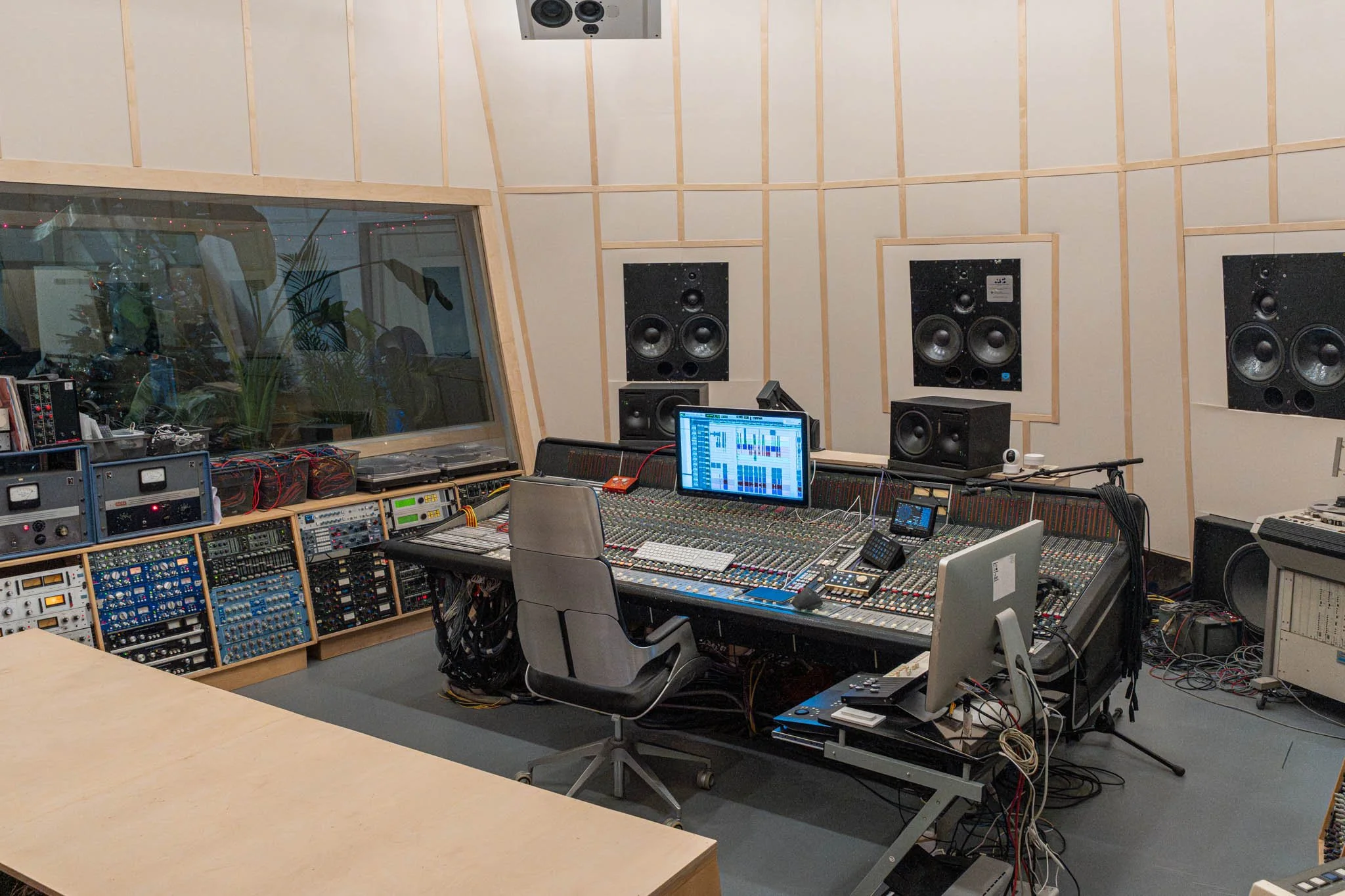 Music recording studio control room with a large mixing console, multiple speakers on the wall, and computer monitors.