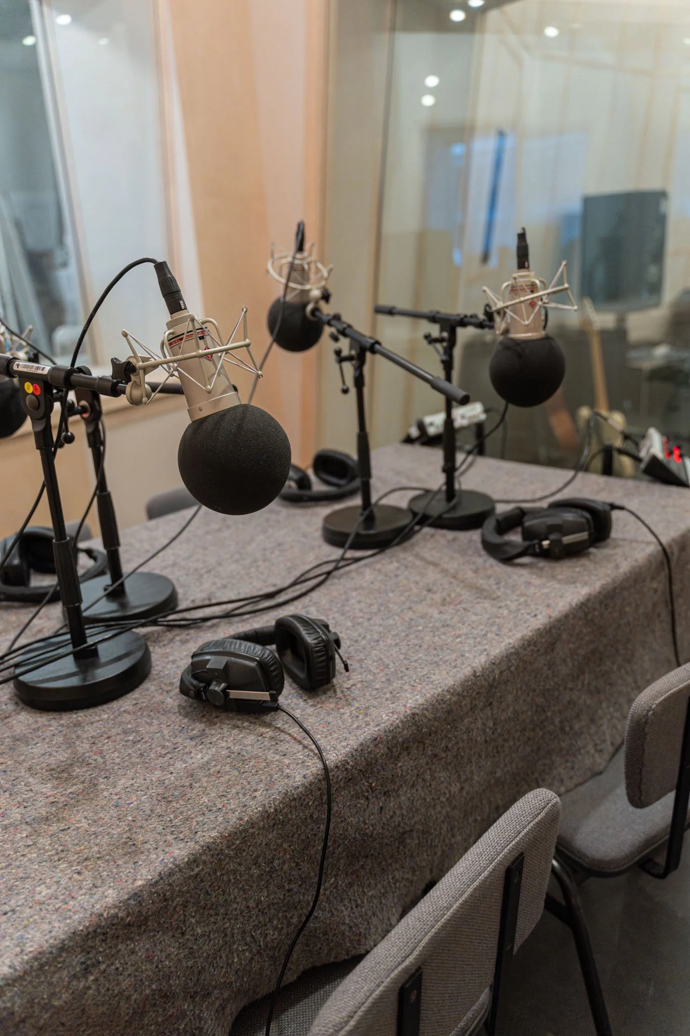 A recording studio setup with three microphones on stands, each with foam windscreens, two pairs of headphones on the table, and a radio on the right side of the table.