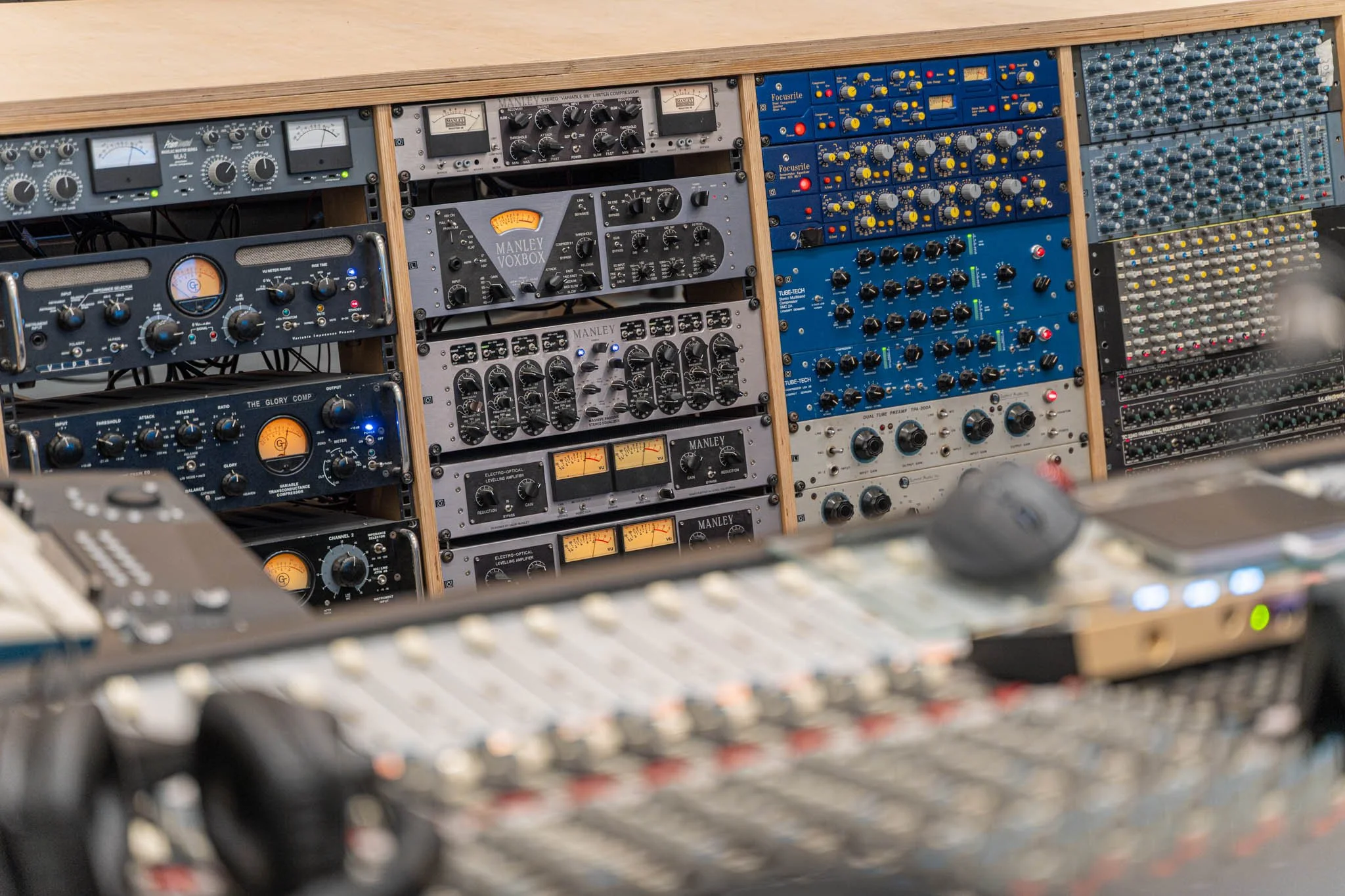 Audio recording studio with various vintage and modern audio equipment and a mixing console in the foreground.
