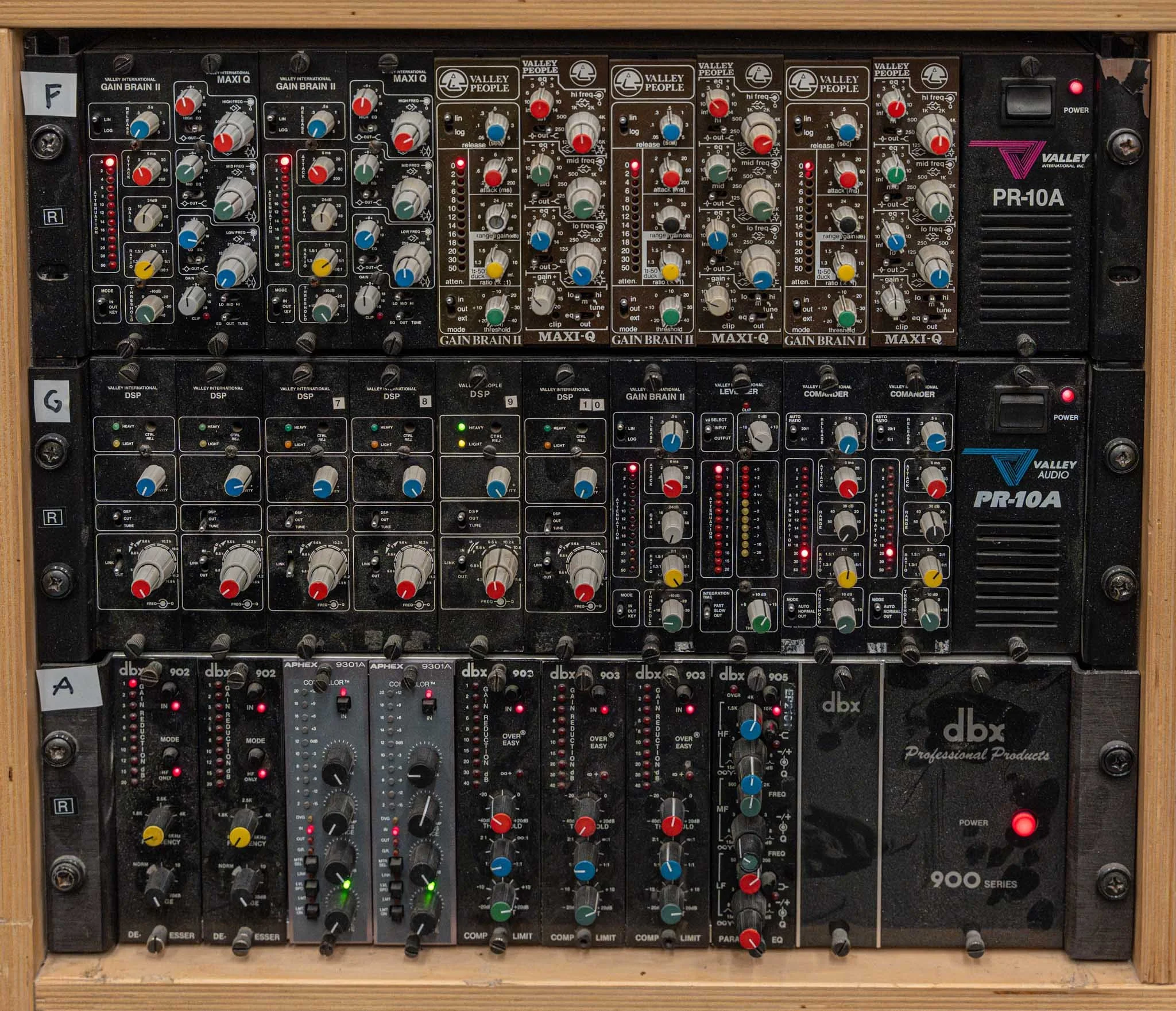 This image shows a professional audio mixer with multiple channels, sliders, and knobs, mounted in a wooden frame. The mixer includes sections labeled Valley People and dbx, with various controls for audio levels, equalization, and effects processing
