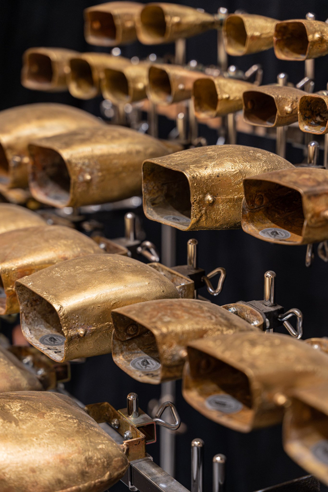 Numerous upside-down metallic molds arranged on a display stand, with some showing rust and texture.