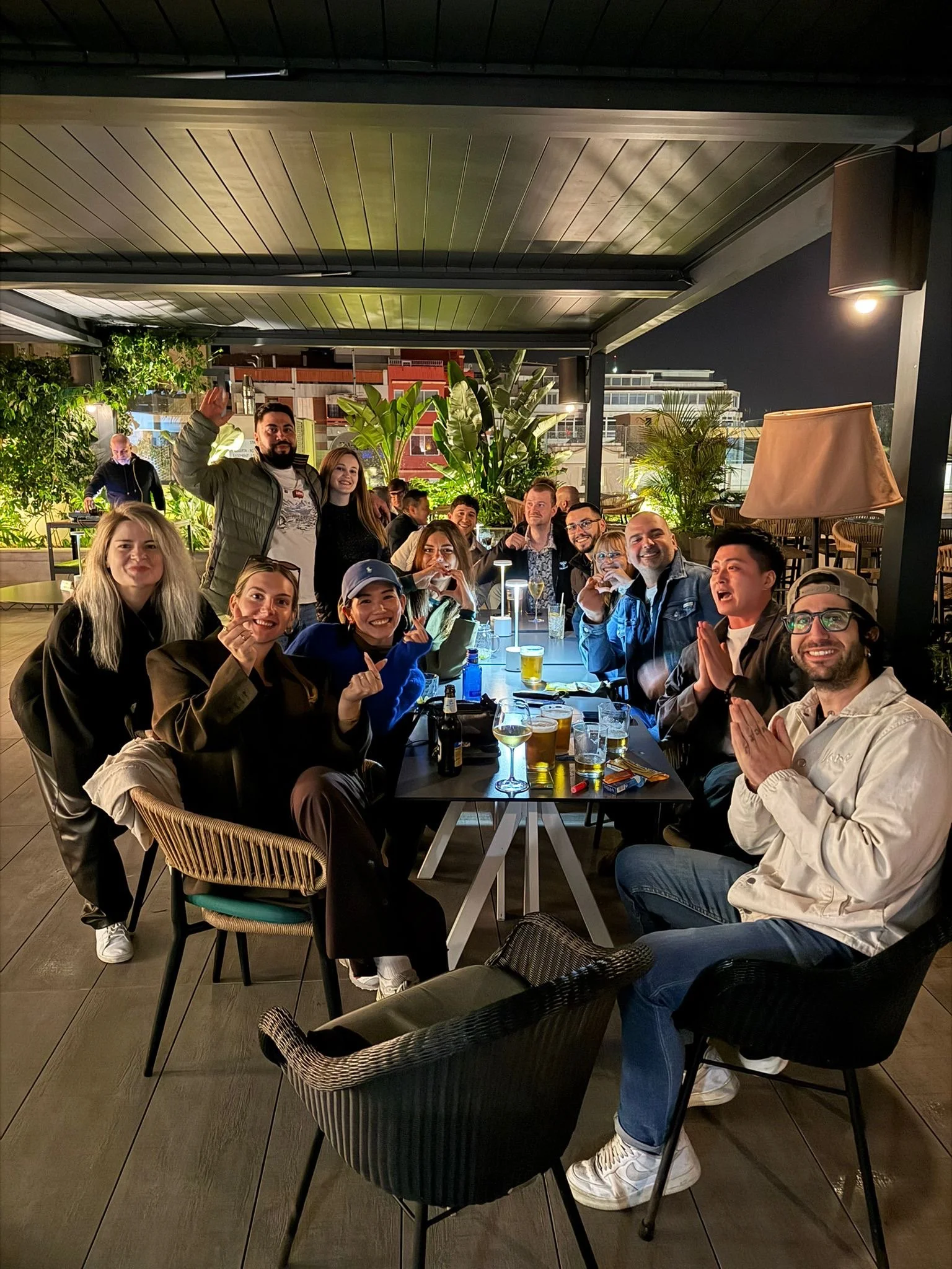 A group of friends enjoying a night out at a rooftop restaurant, sitting around a table with drinks, smiling, and posing for the photo.