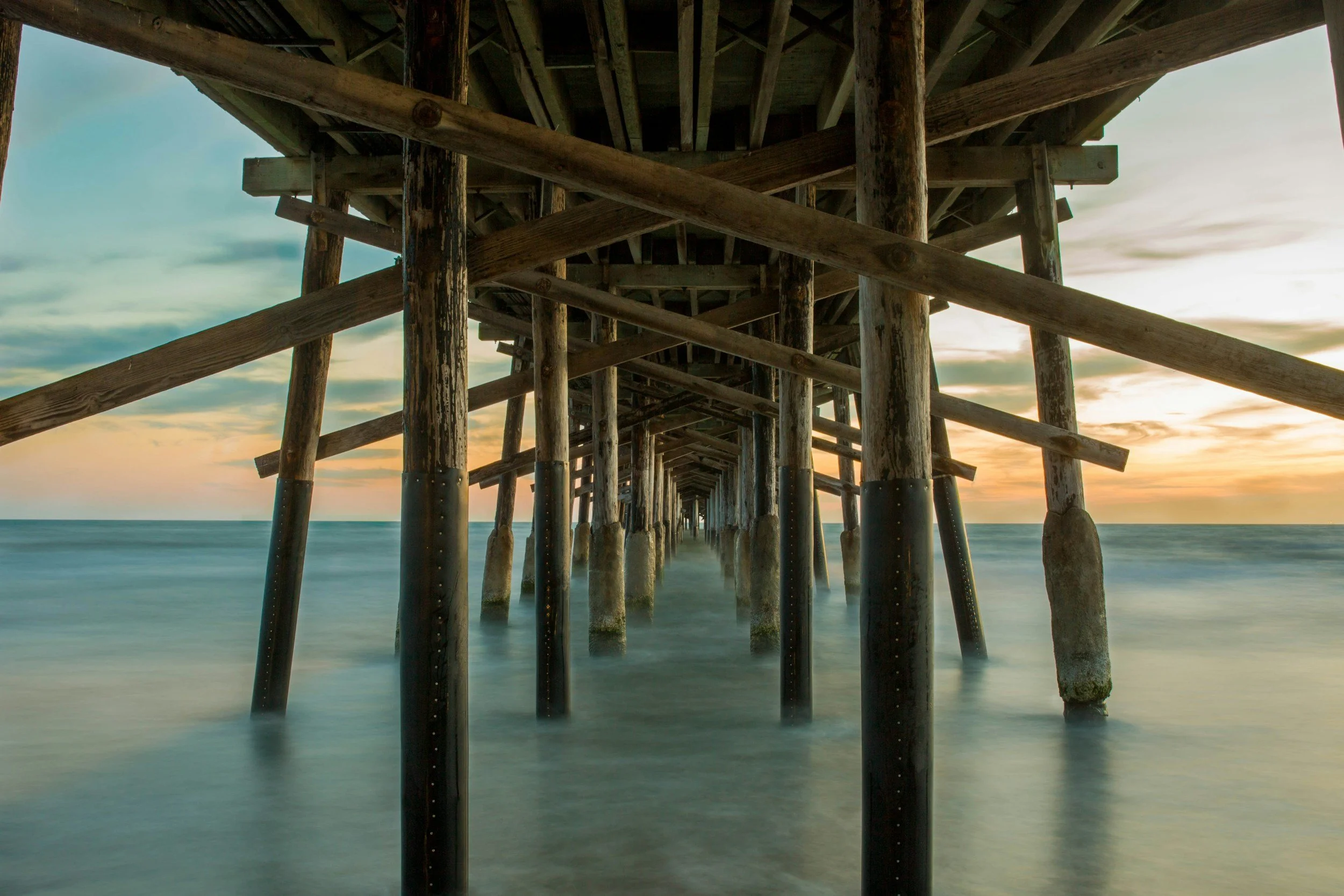View of a wooden pier extending over the ocean at sunset, with calm water and a partly cloudy sky.