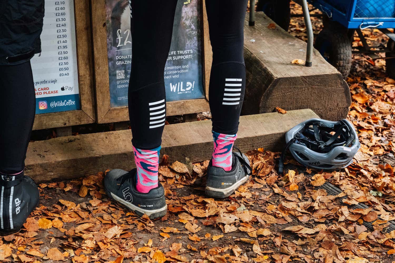 Person getting ready for Wild About Running, wearing black athletic leggings with white stripes, pink camouflage socks, and black athletic shoes, standing on a woodland floor.