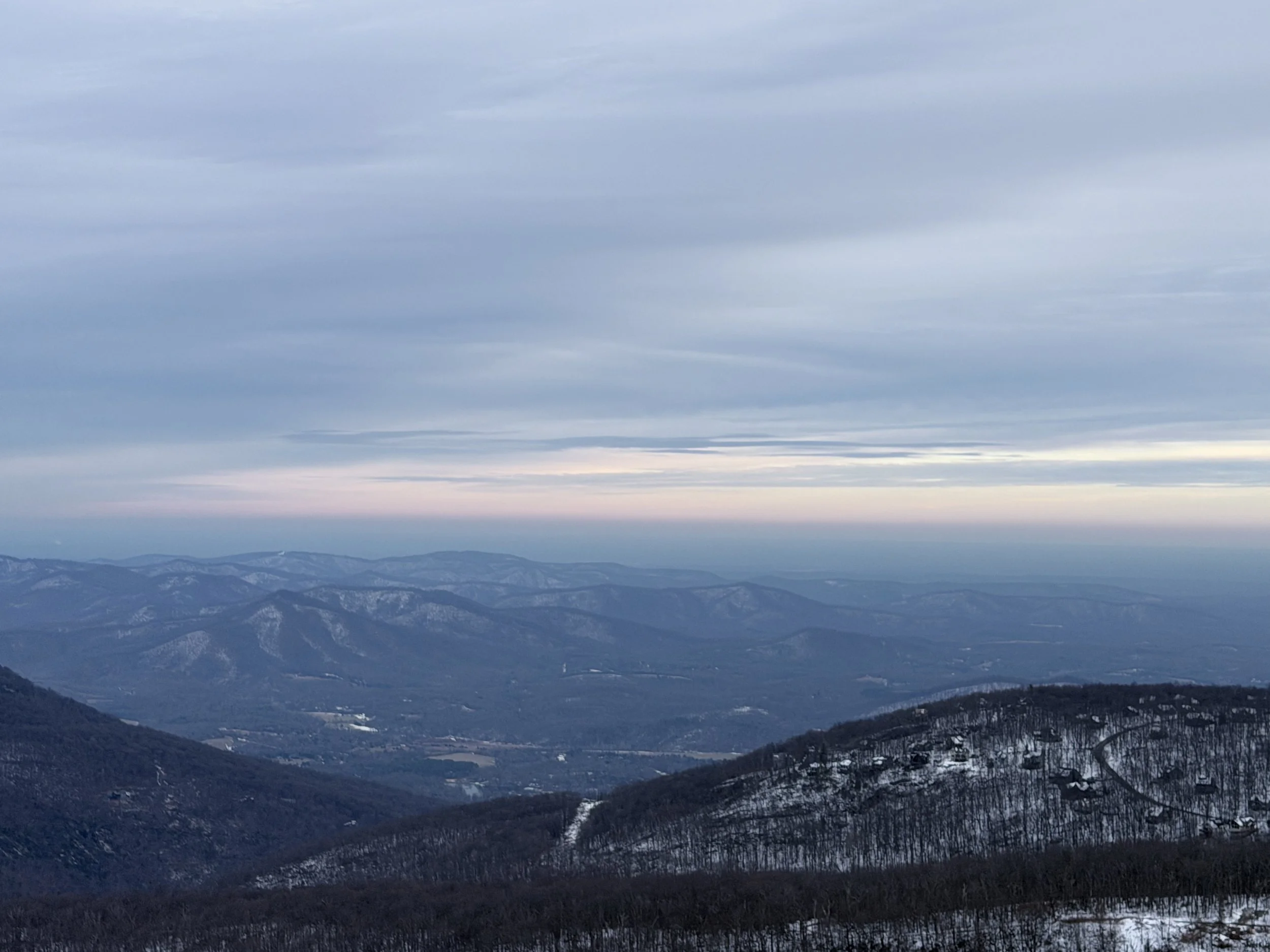 A mountain landscape with snow-covered hills and a cloudy sky during dusk.