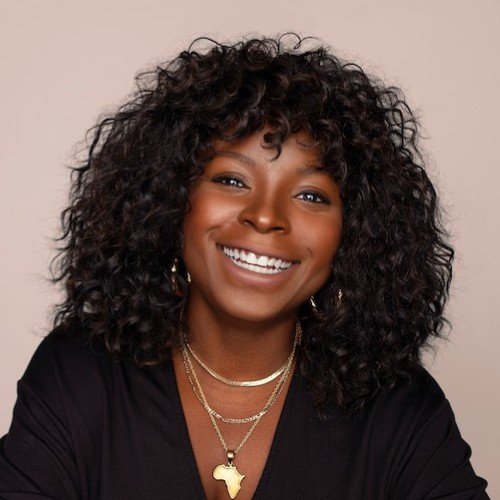 A woman with dark, curly hair smiling, wearing a black top and layered gold necklaces with an Africa-shaped pendant.