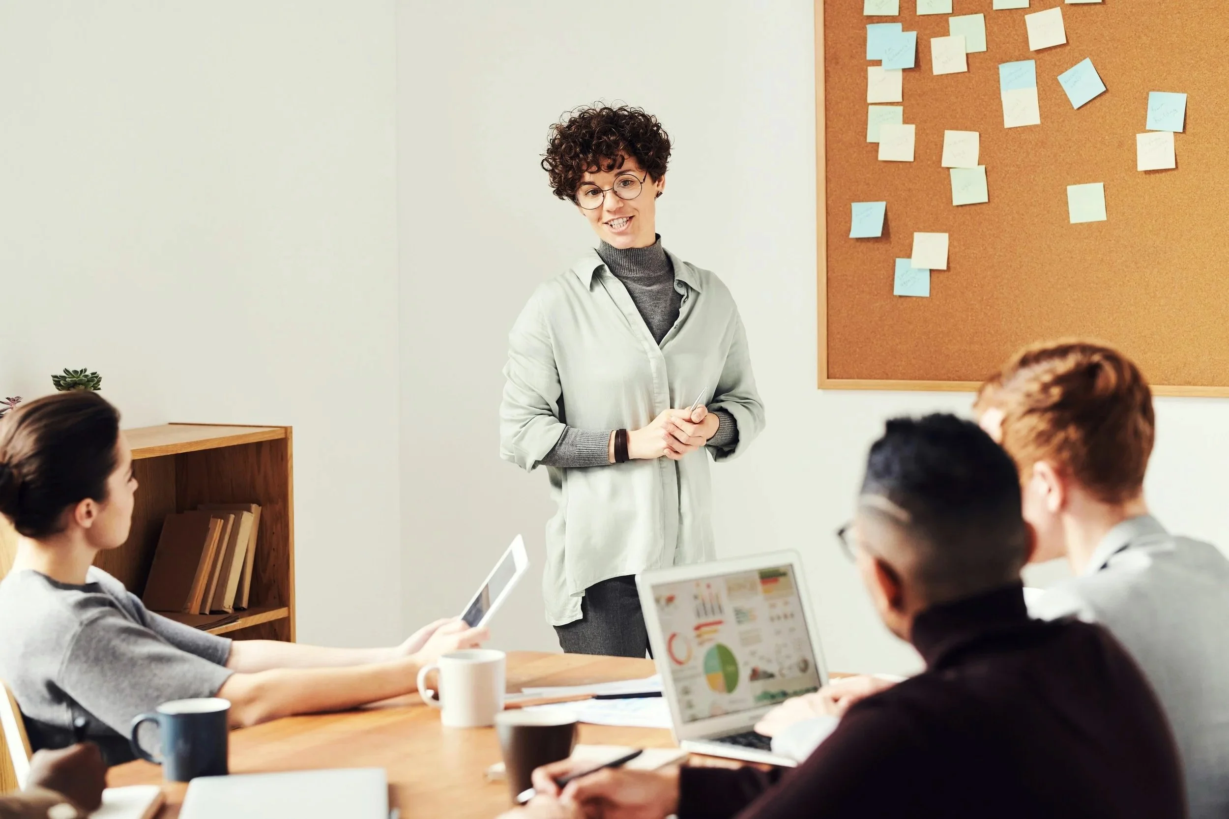 A woman standing at a meeting table speaking to a group of people in a conference room.