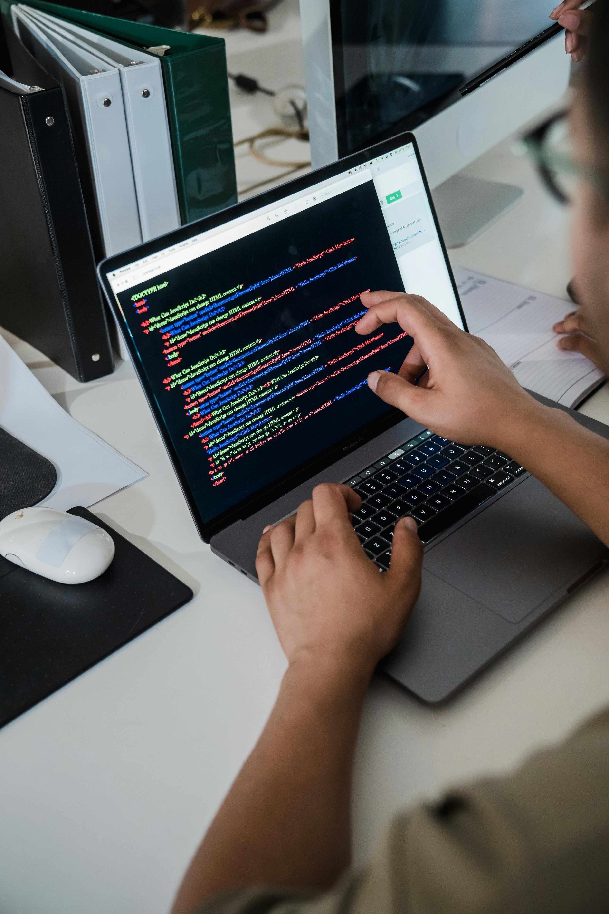 Database Programming - Person working on a laptop with colorful code on screen in a tech office.