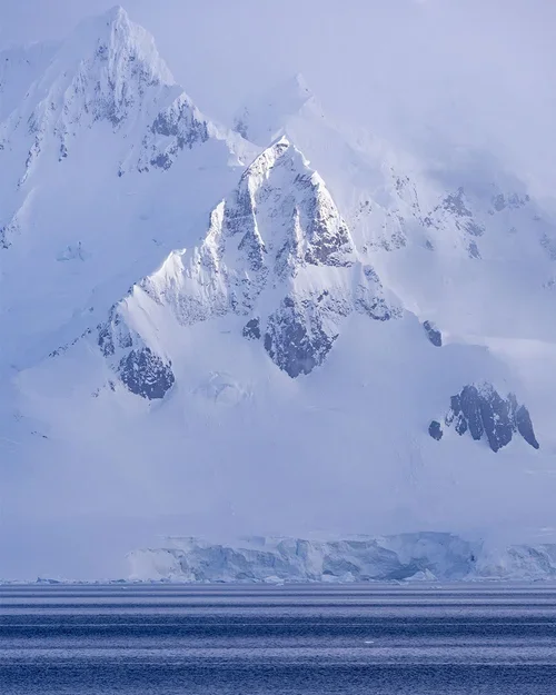 Snow-covered mountain peaks with an icy blue ocean in the foreground.