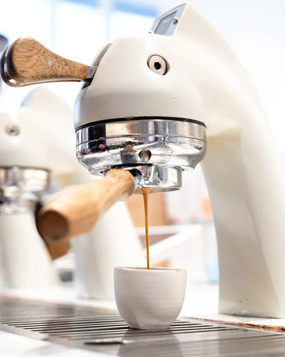 Close-up of a vintage espresso machine in use, pouring coffee into a small white ceramic cup.