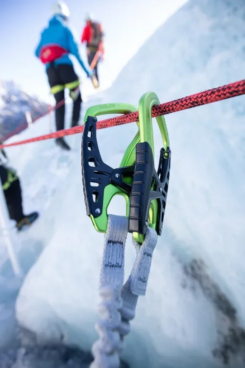 Climbing tools clipped onto a red rope on snowy mountain, with climbers in the background.