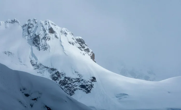 Snow-covered mountain peak with rugged, icy slopes and a cloudy sky.