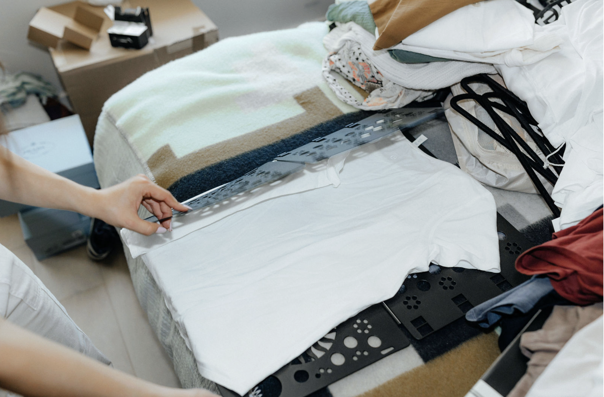 Person folding a stack of clothes on the floor, with various folded clothing items including pants, shirts, and undergarments.