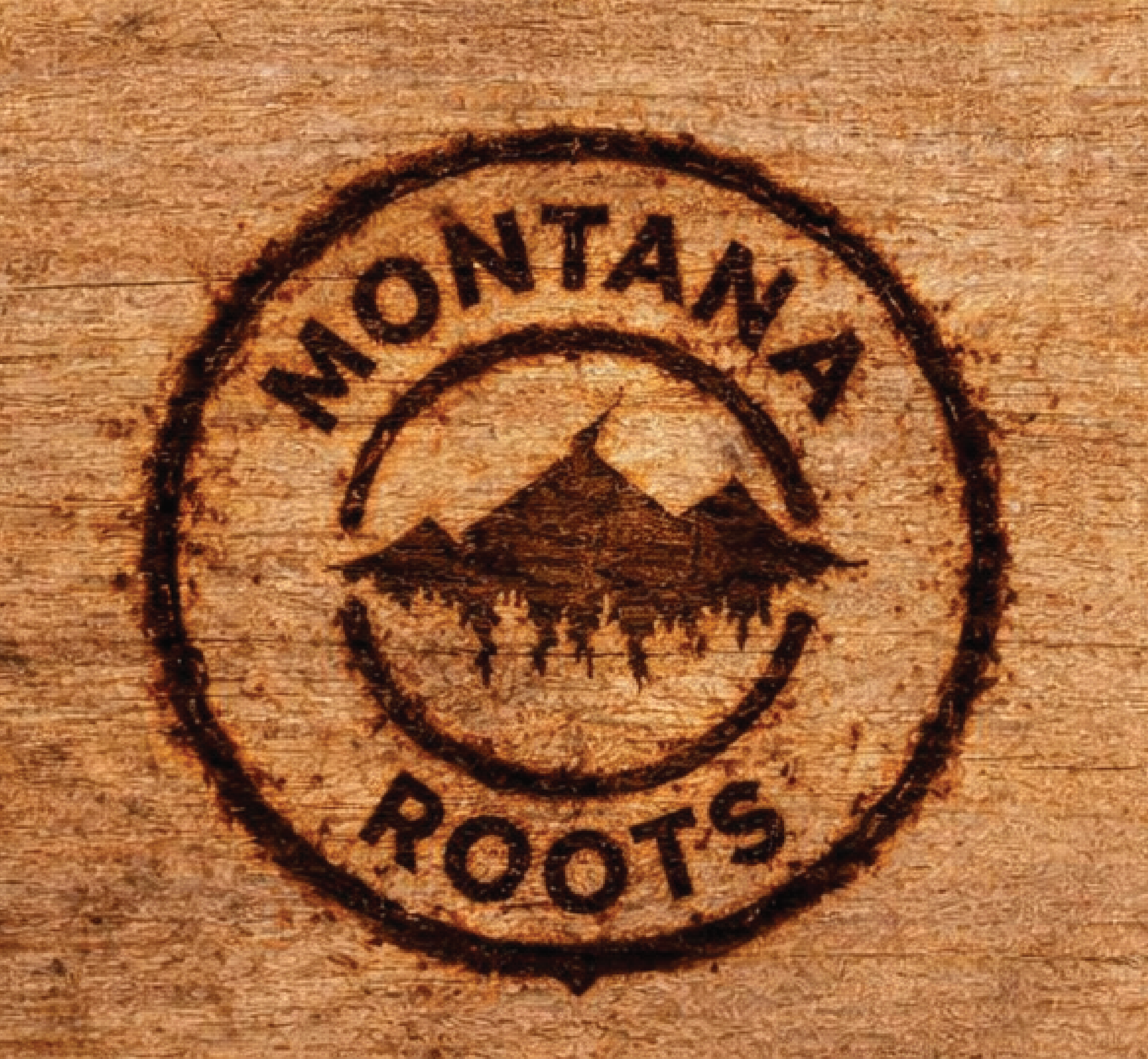 Wooden surface with a circular logo engraved that reads 'Montana Roots' and features a silhouette of mountains and a forest.