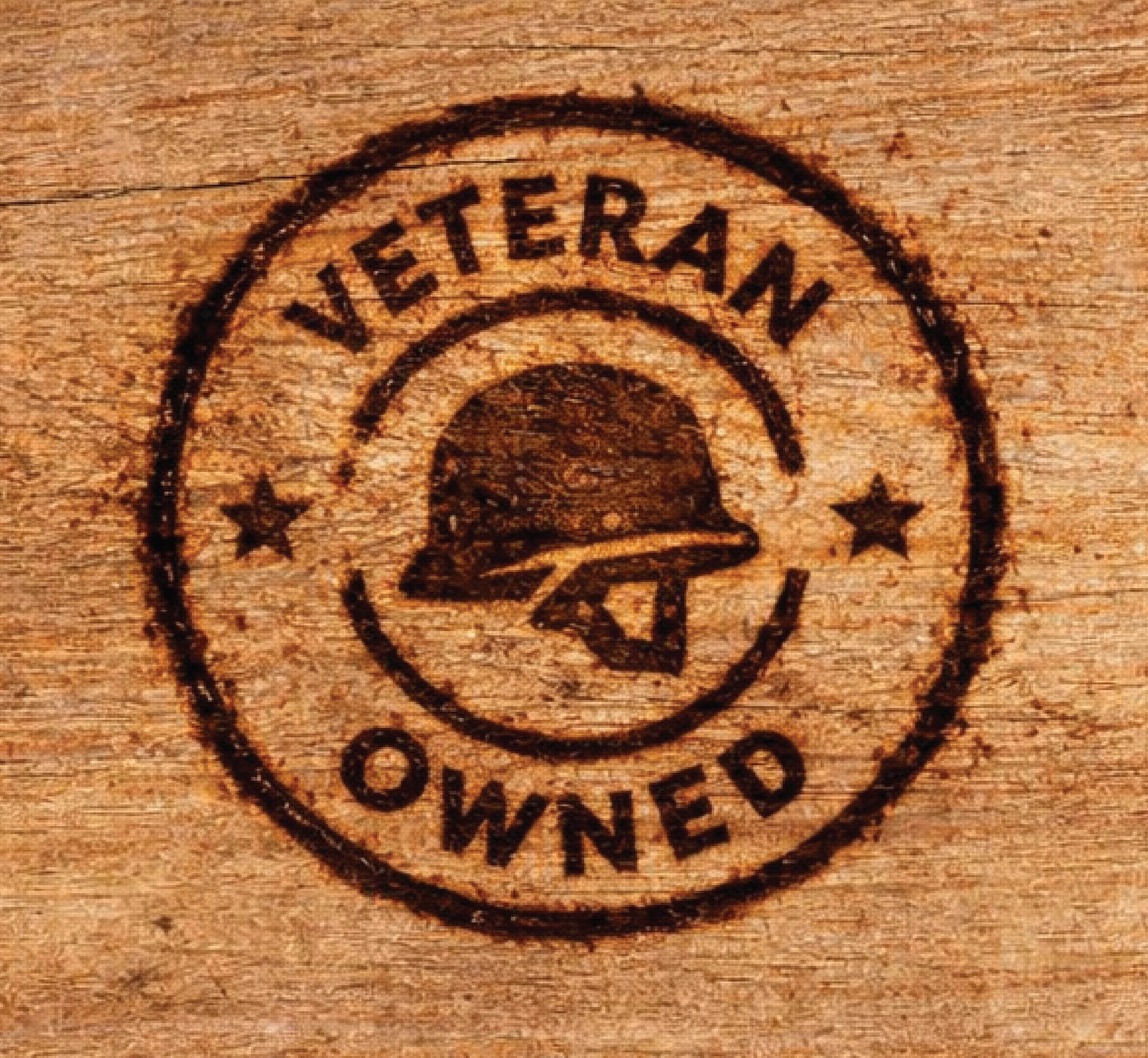 A circular stamp on wood with the words 'VETERAN' at the top and 'OWNED' at the bottom, featuring a helmet in the center.