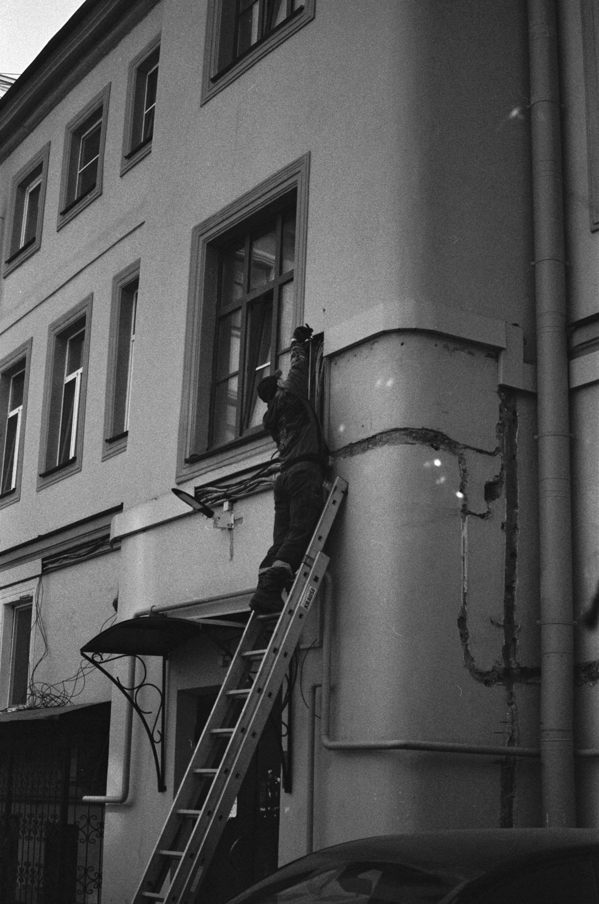 A worker standing on a ladder inspecting the exterior of a commercial building.
