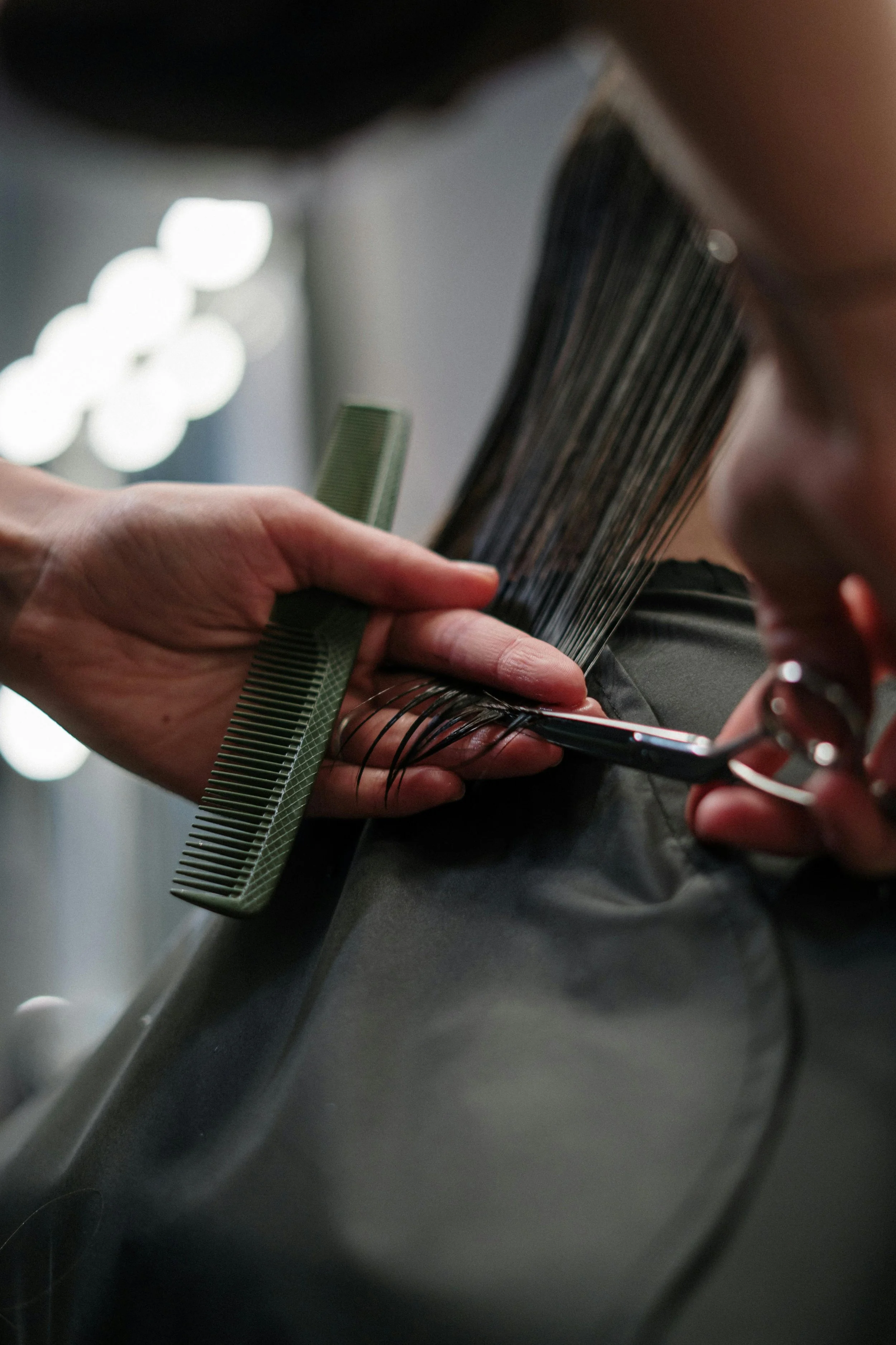 A hairstylist trims a client's hair with scissors, a comb, and hair clips in a salon.