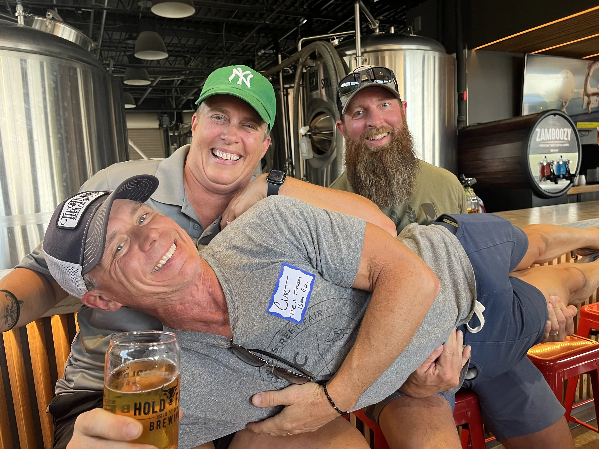 two smiling people are holding a third smiling person horizontally while that person is holding a beer.