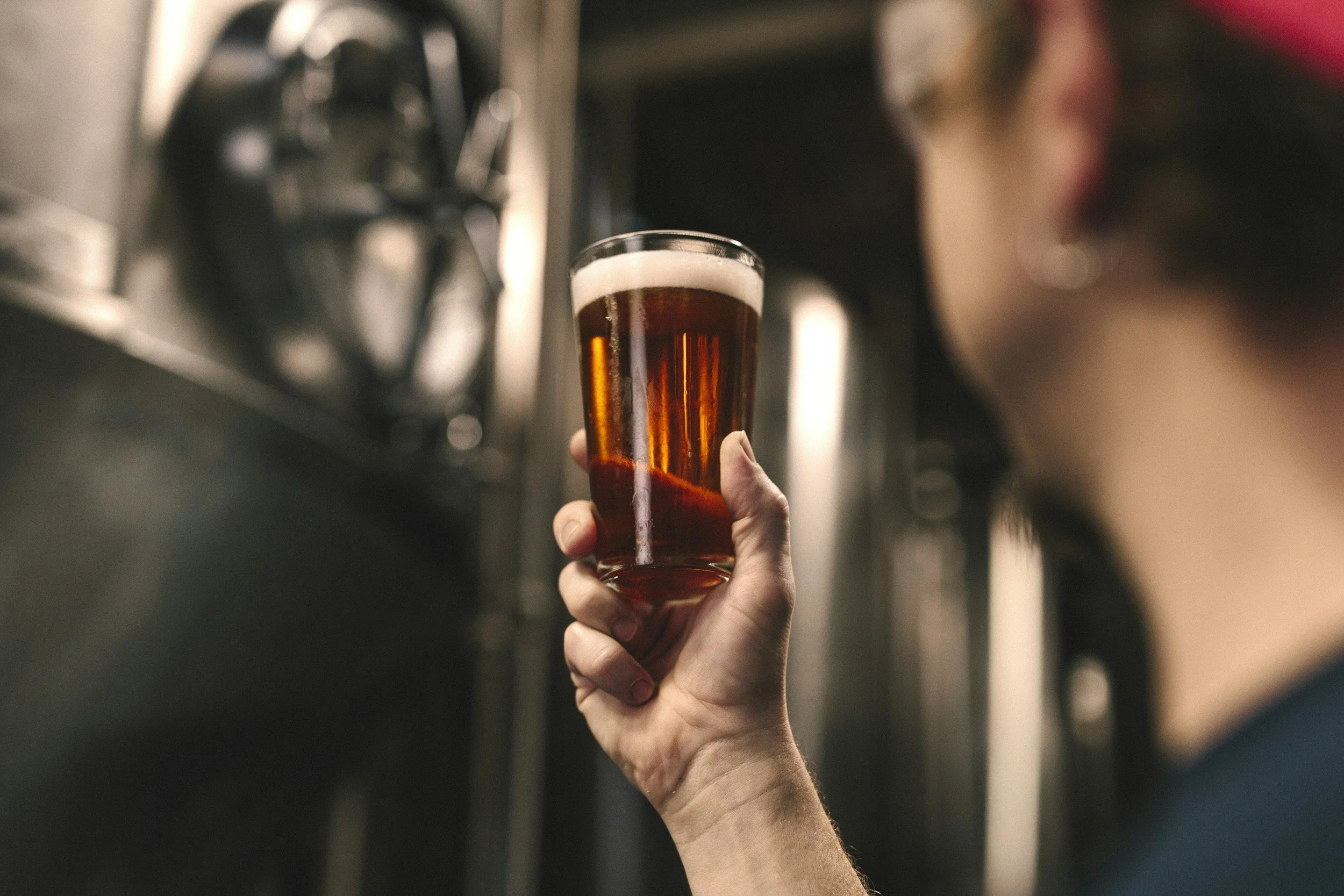 man holding up a glass of beer to inspect the color of the liquid