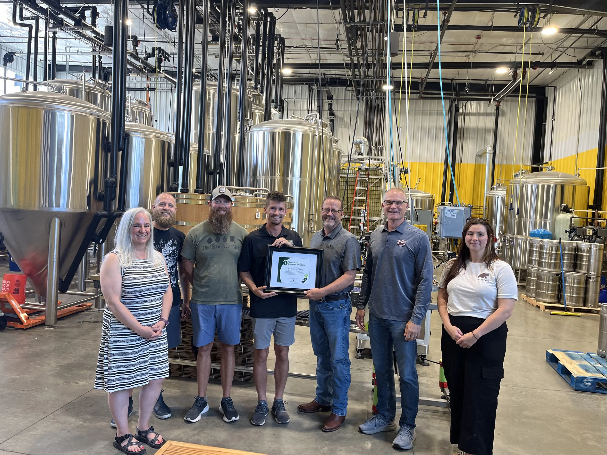 group of women and men posing in a brewery holding a mo green brewing certification plaque