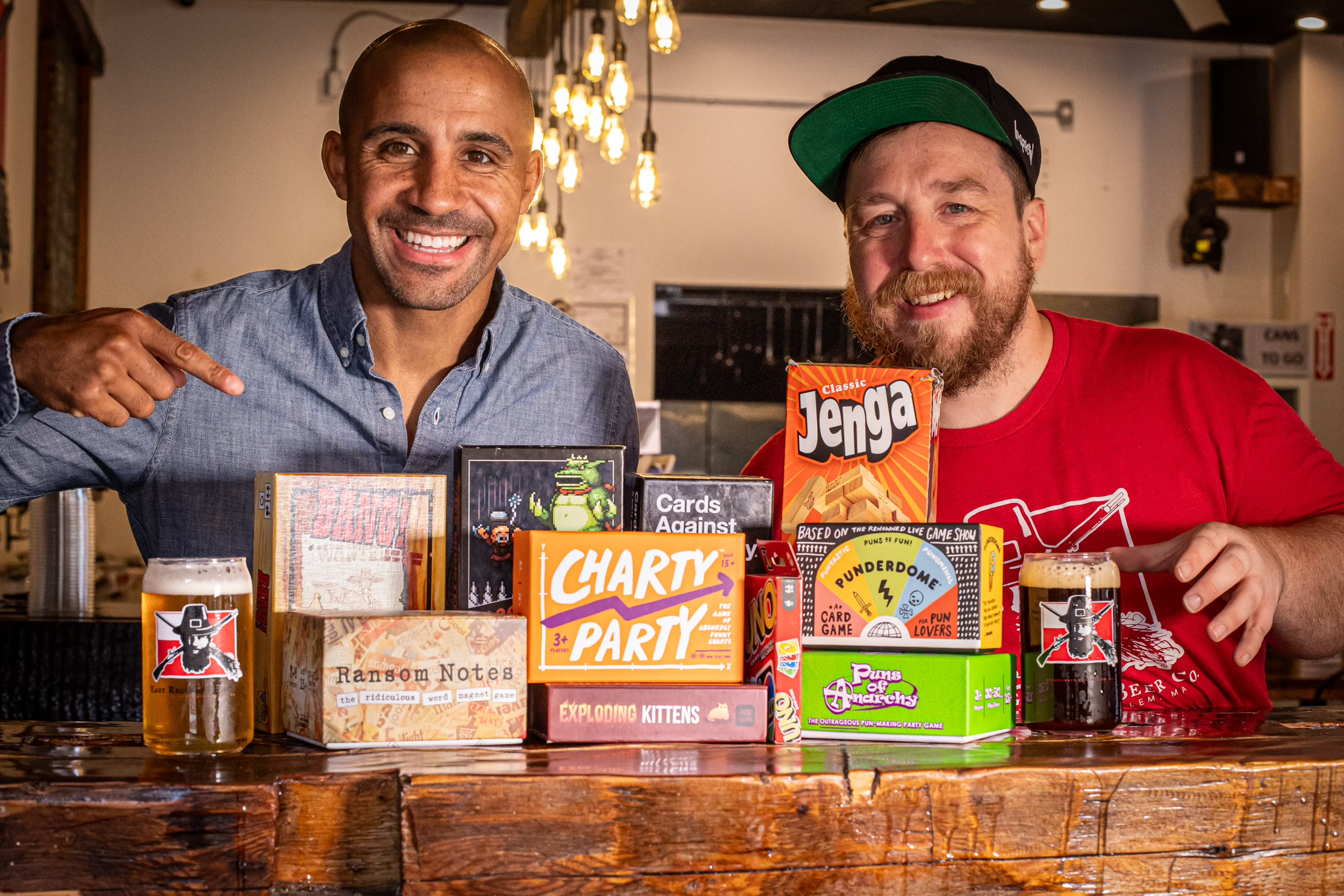 two men behind a bar with a group of various board games available