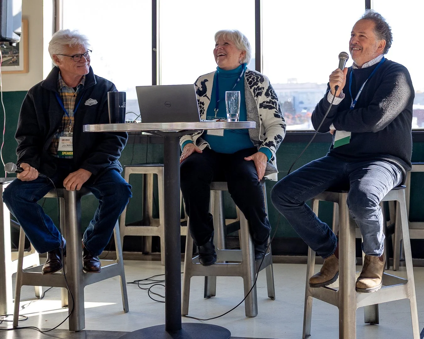 three panel speakers sitting around a high top table with microphones addressing the room