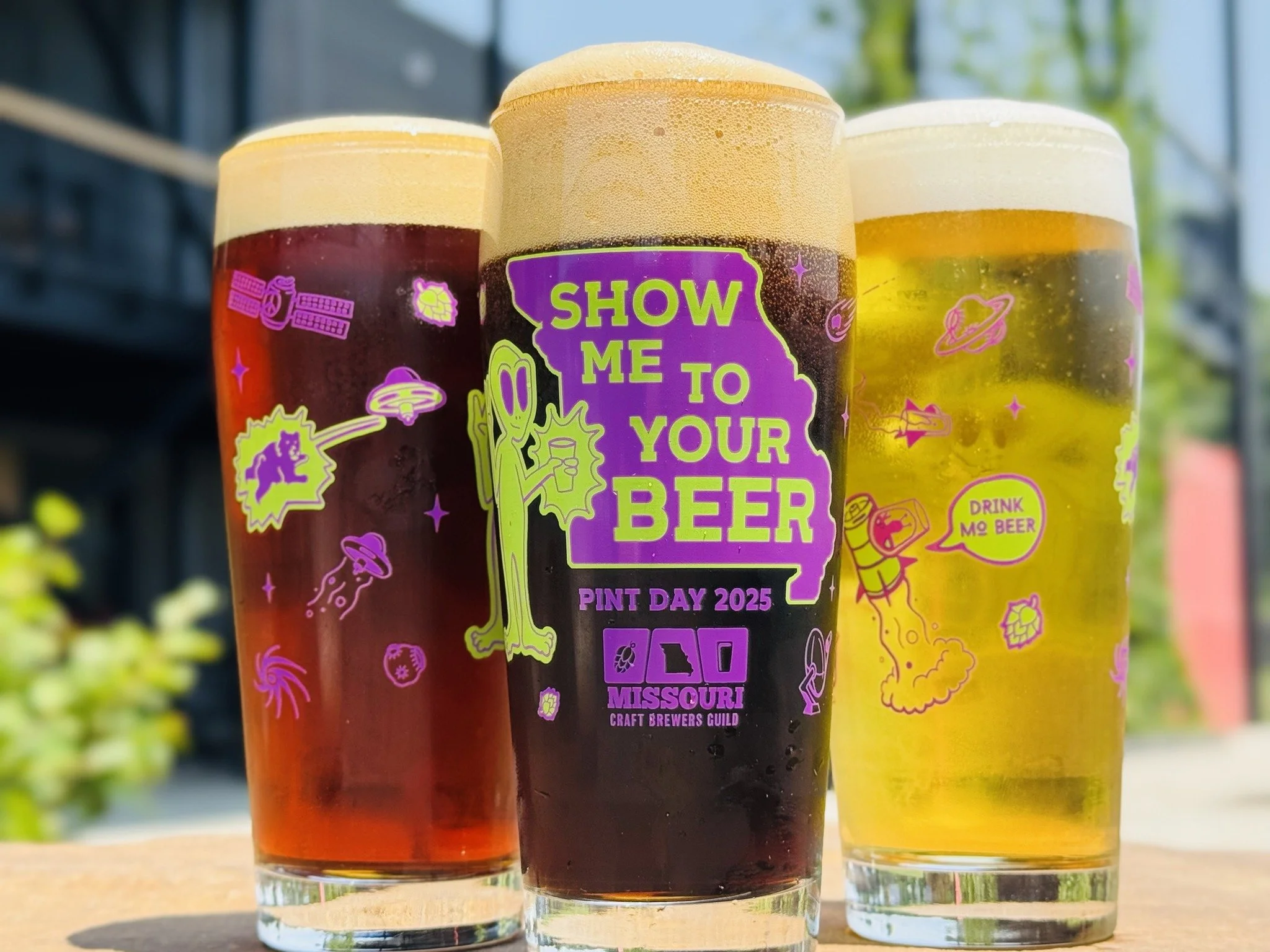 three pint day glasses each holding a different style of beer evident by the color of the liquid, angled to showcase the various designs featured around the glass