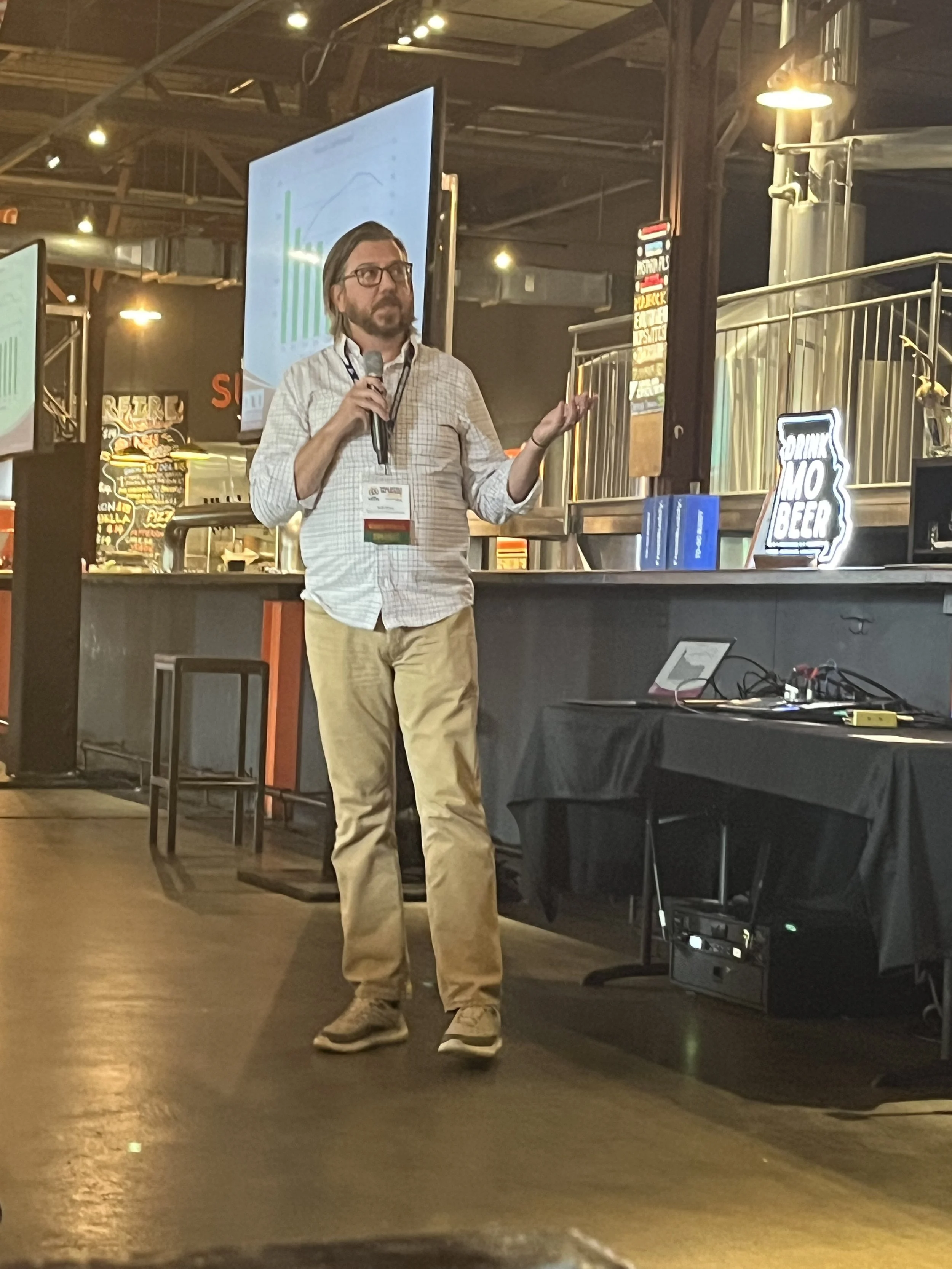 a man with a microphone gestures to a screen displaying a graph of beer industry data