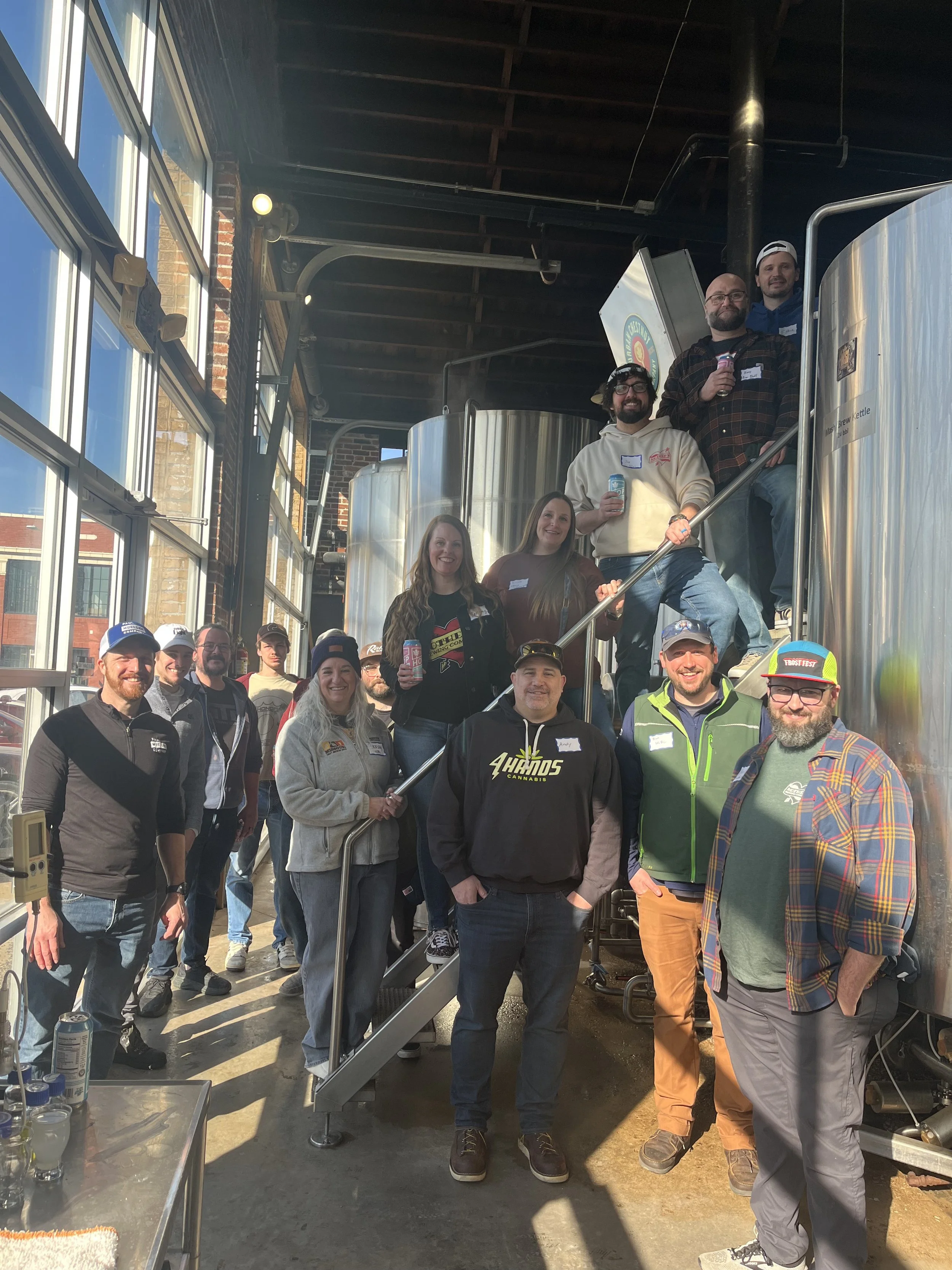 Group of brewers pose on the brew deck next to the stainless steel tanks