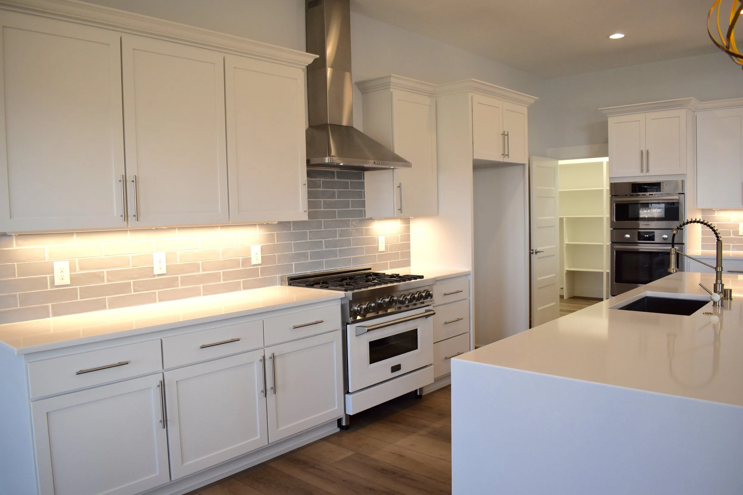 Before staging. Modern kitchen with white cabinets, stainless steel appliances, gray subway tile backsplash, white countertops, and a large island with a black sink and gooseneck faucet.