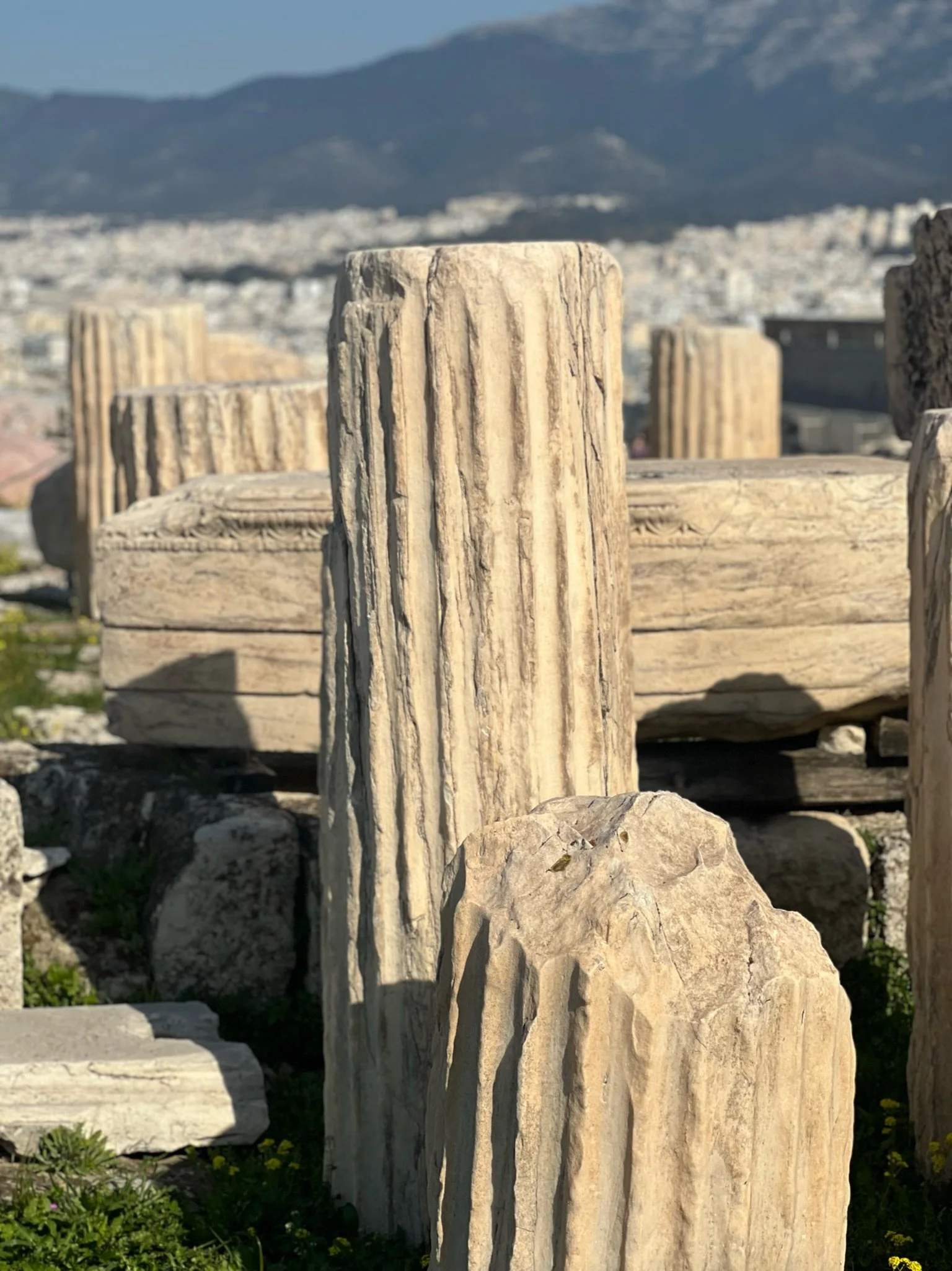 Close-up of ancient marble or limestone columns with fluted design, placed outdoors with a mountainous landscape in the background.