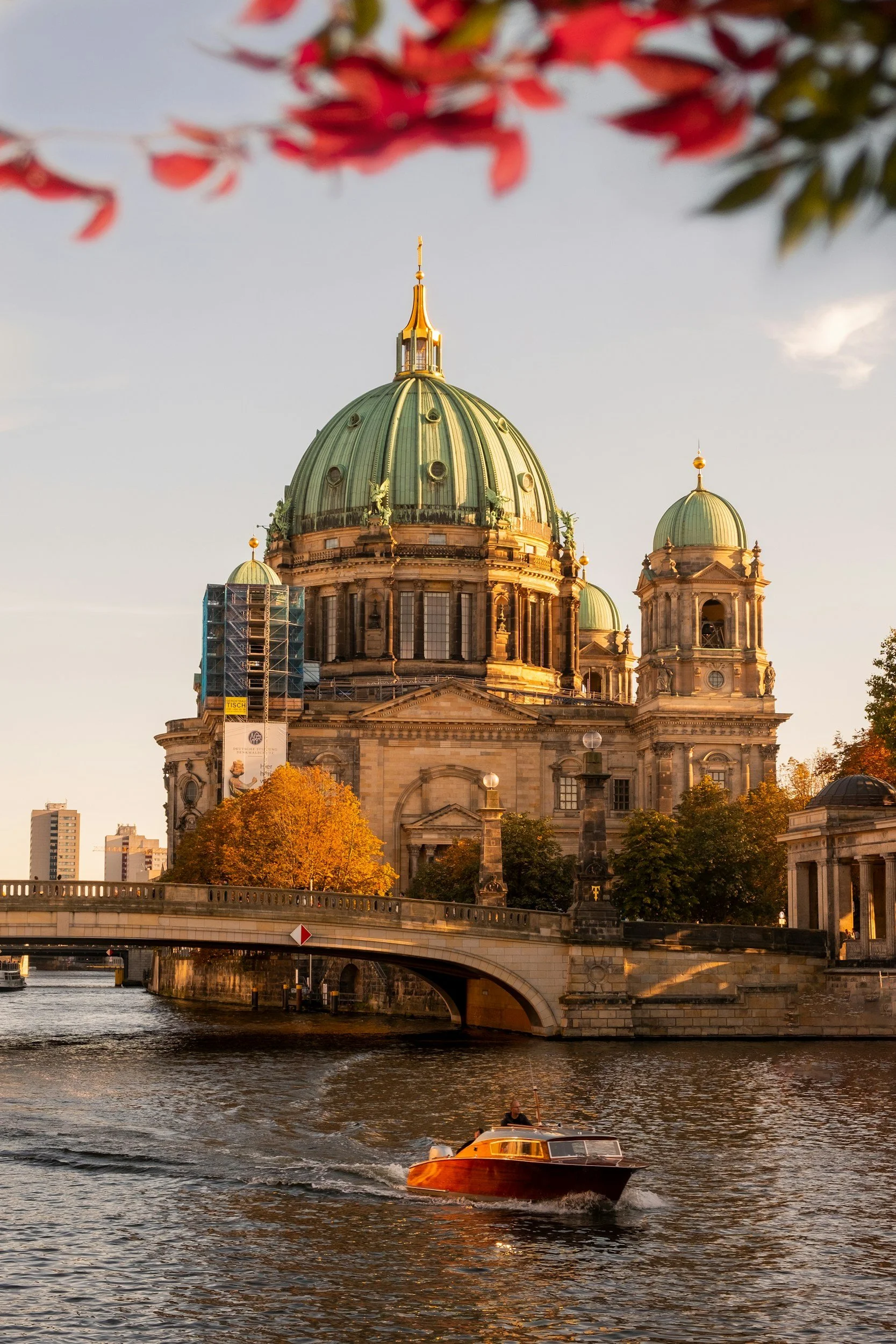 A boat sailing on the river near Berlin Cathedral with autumn trees in the background during sunset.