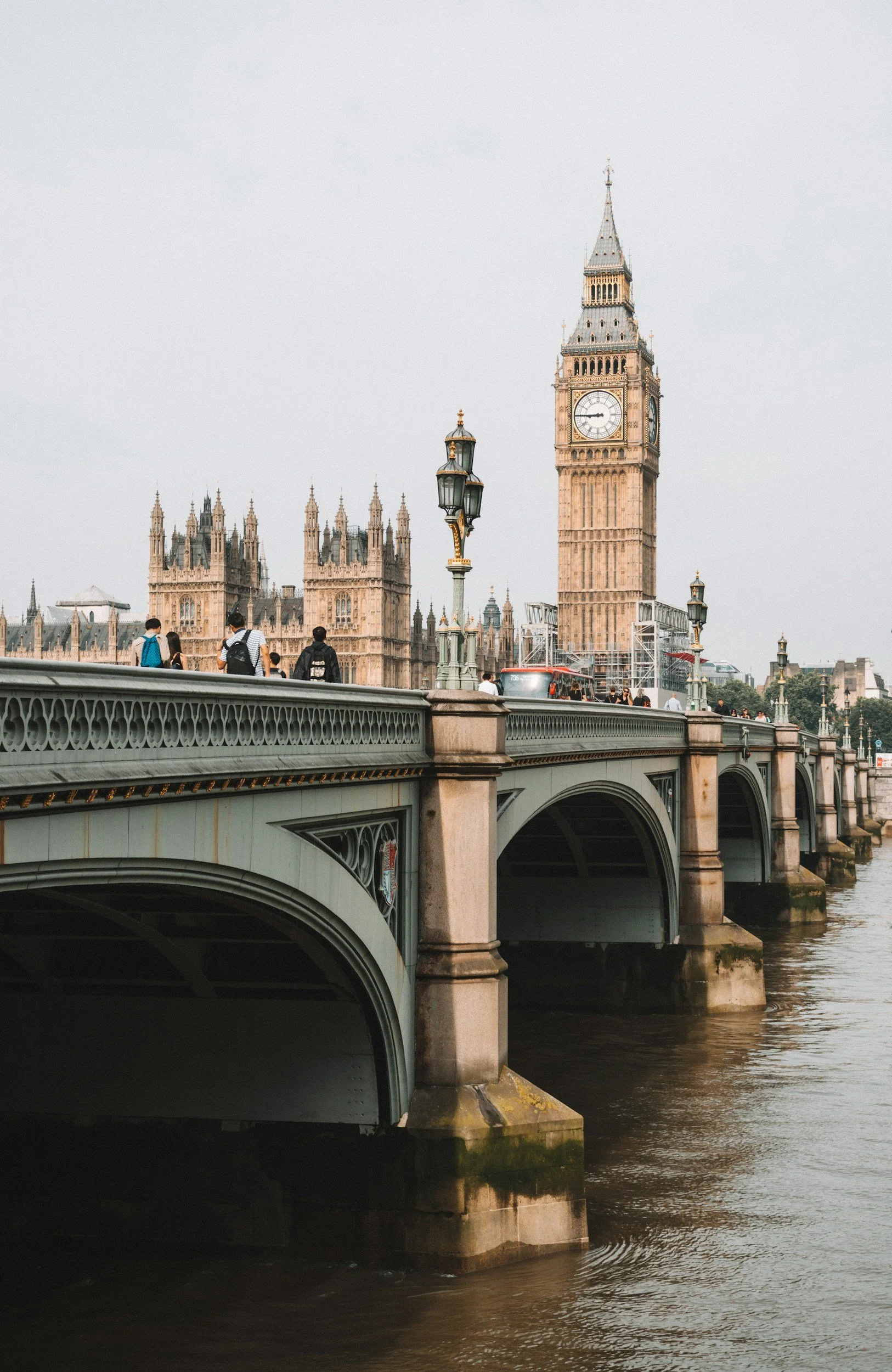 London skyline featuring Big Ben and the Houses of Parliament viewed across the Thames River, with pedestrians walking on Westminster Bridge.