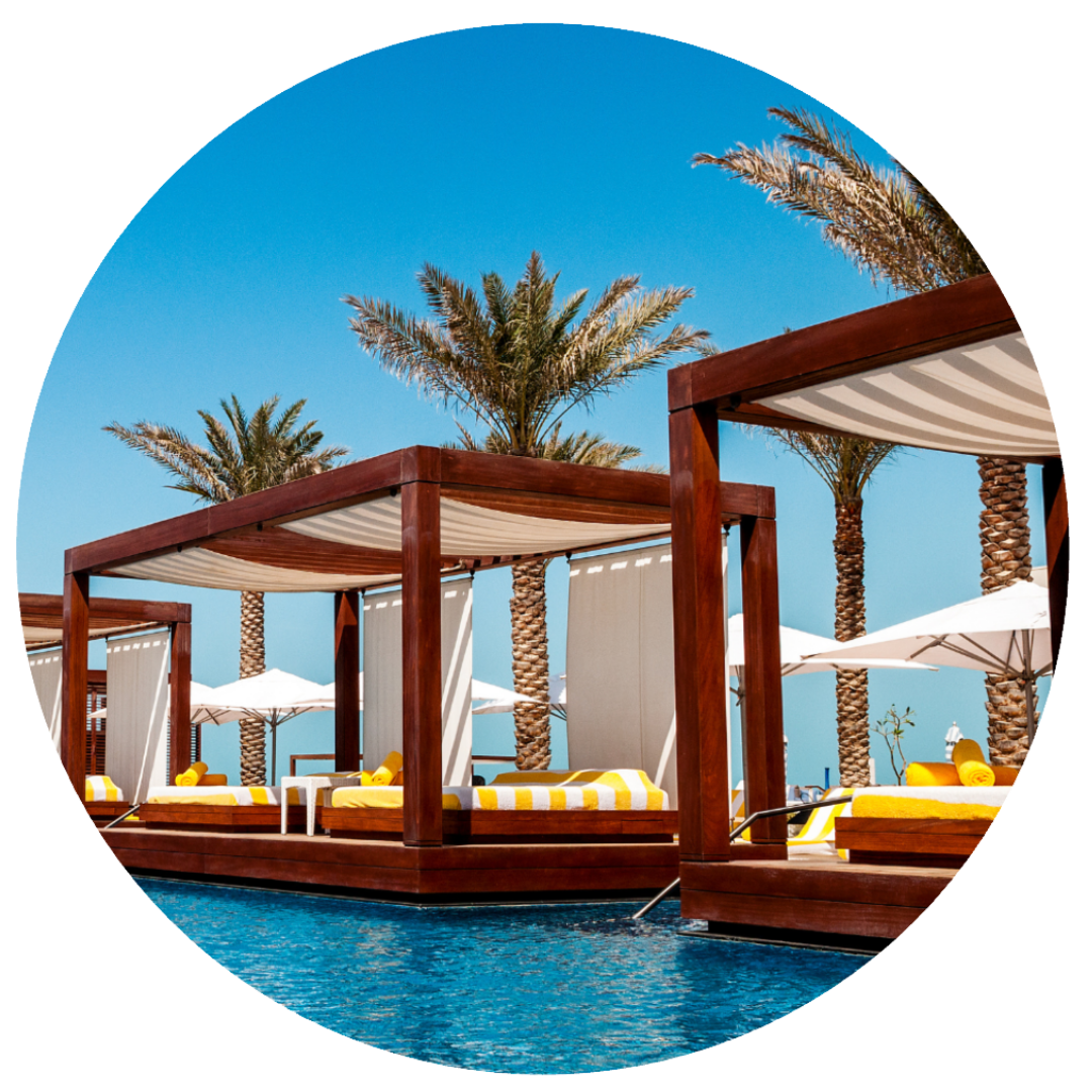 Luxury poolside cabanas with yellow and white striped cushions, palm trees, and white umbrellas under a clear blue sky