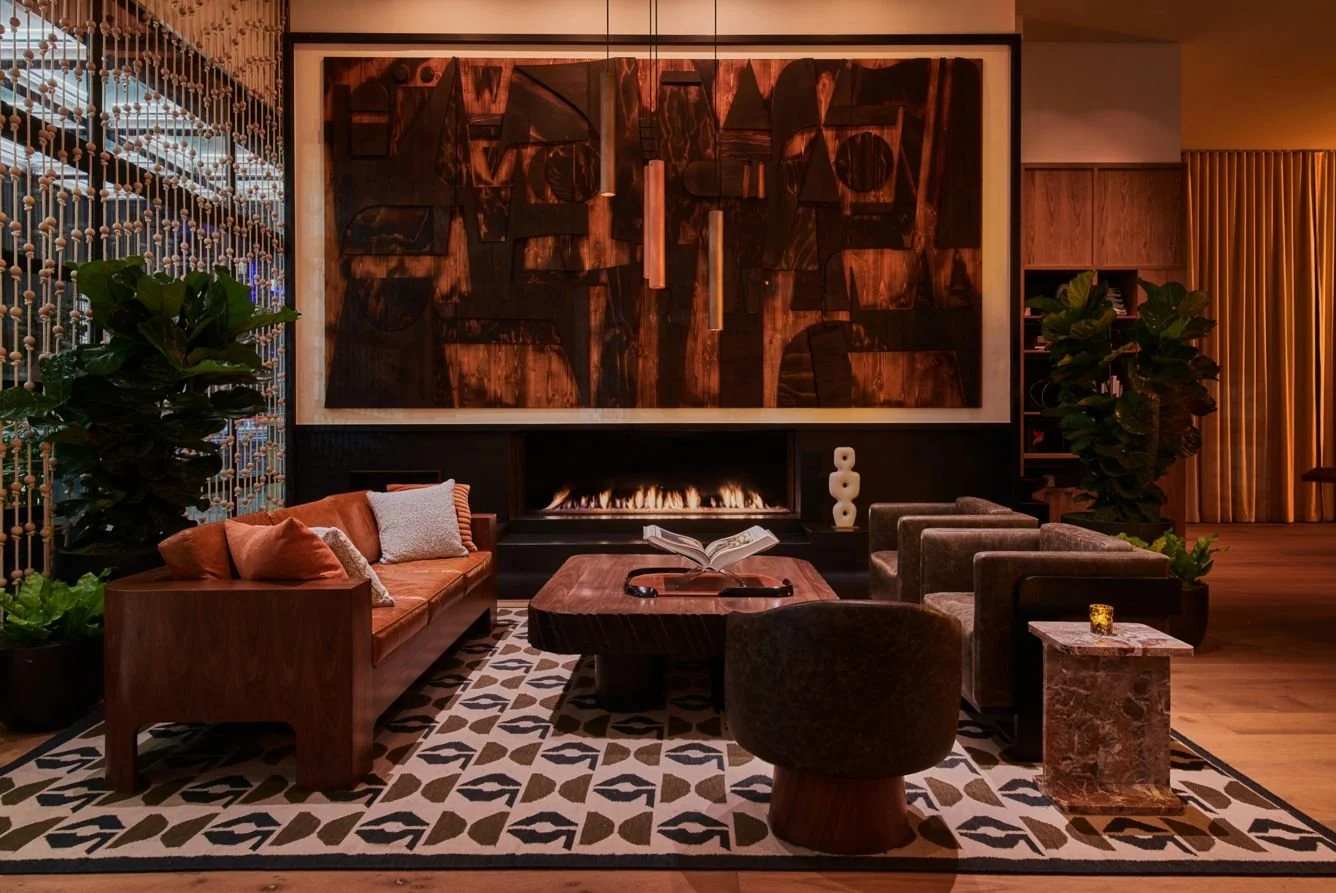 Luxurious living room with modern furniture, a fireplace, large abstract wooden art, potted plants, and patterned rug.