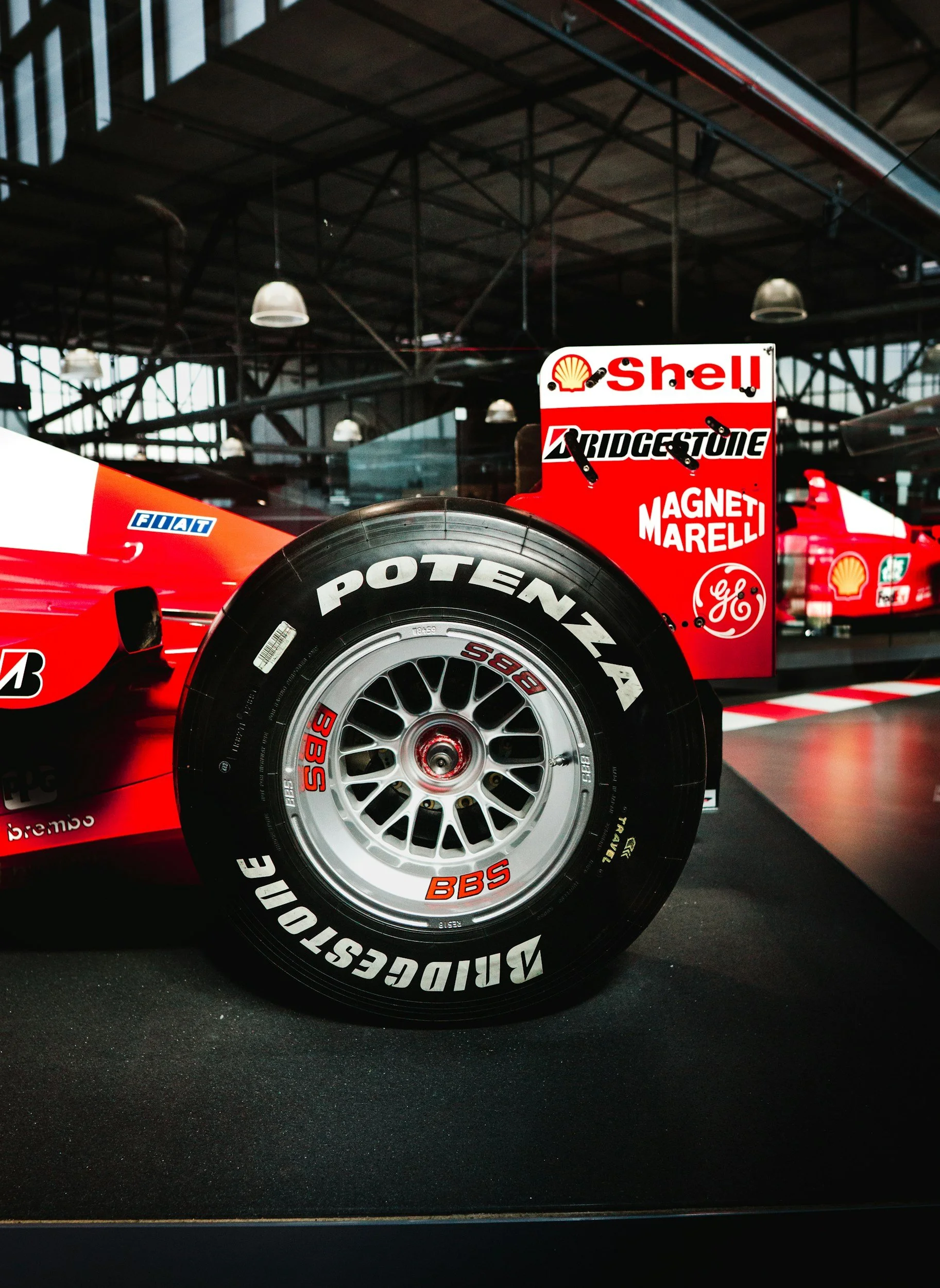 Close-up of a Formula 1 car wheel with Bridgestone Potenza tires, displayed indoors with sponsor stickers like Shell, Bridgestone, Magneti Marelli, and GE visible nearby.