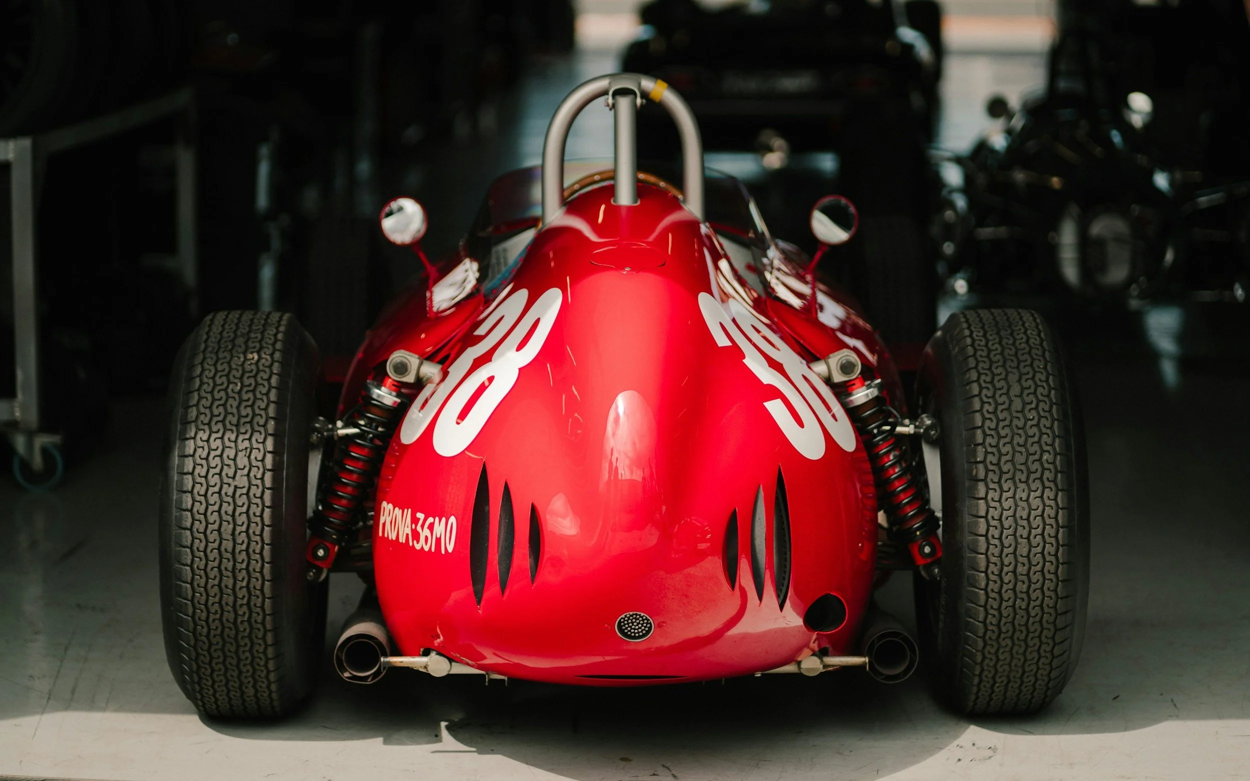 Red vintage race car with the number 20 on the hood, parked inside a garage.
