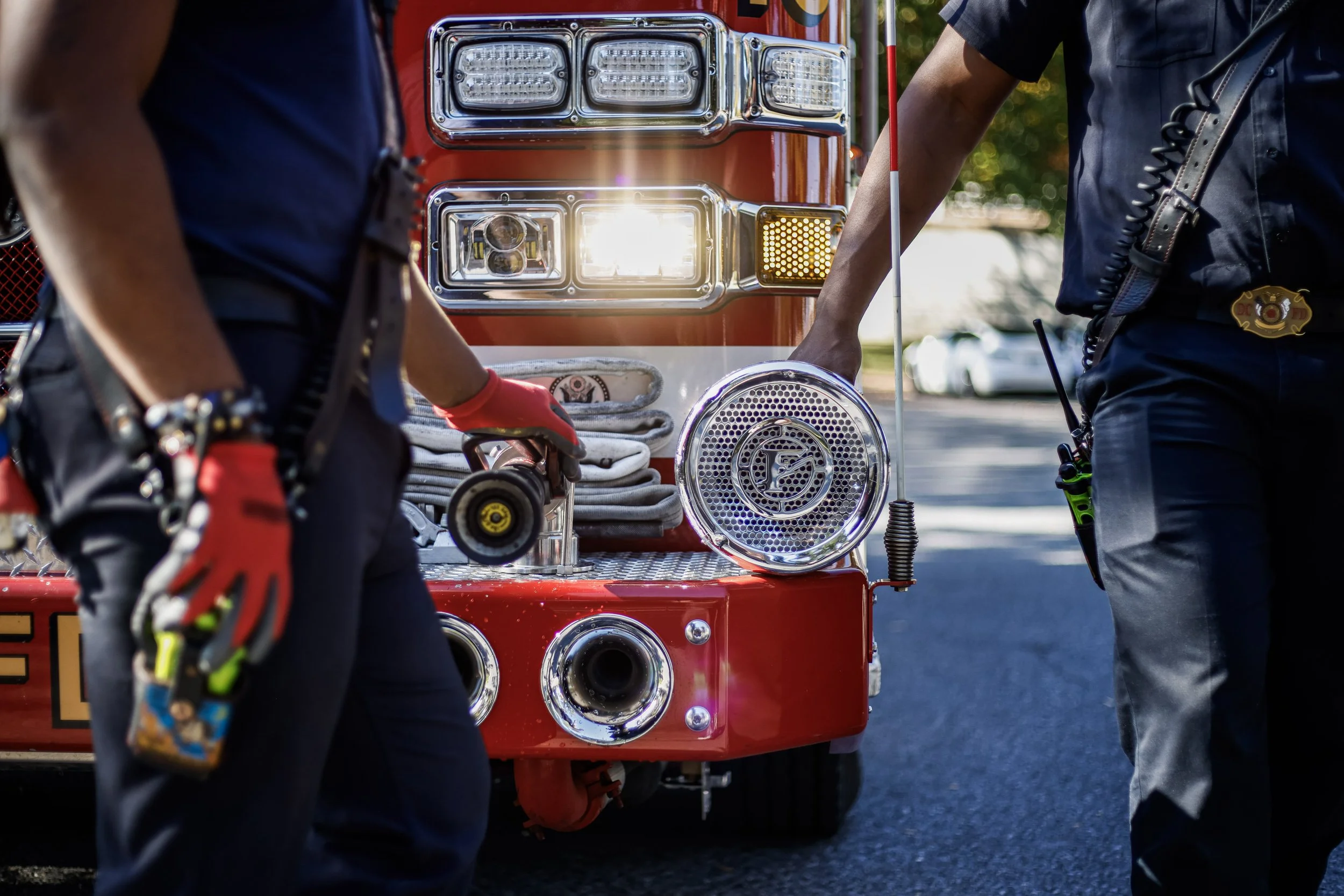 Two emergency responders inspecting the front of a red fire truck with multiple lights and sirens.