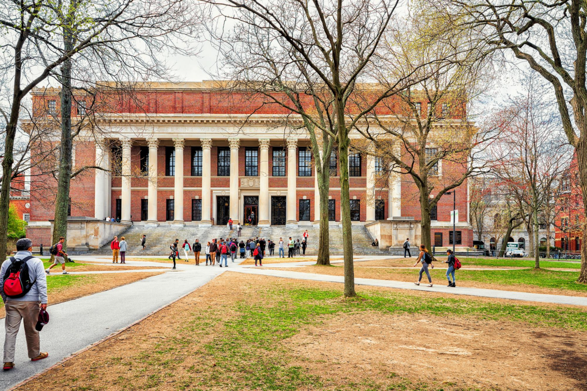 Students walking on the yard in front of a university building with tall columns and brick facade