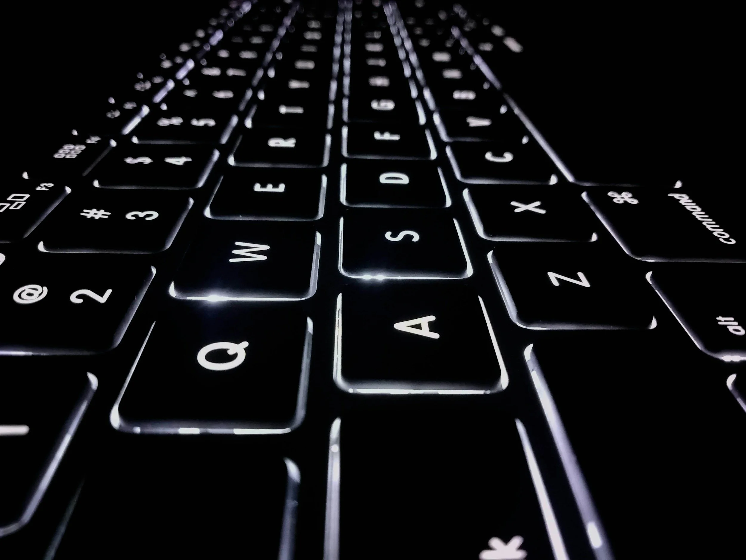 Close-up of a backlit computer keyboard at night, showing the letter keys from W to X.
