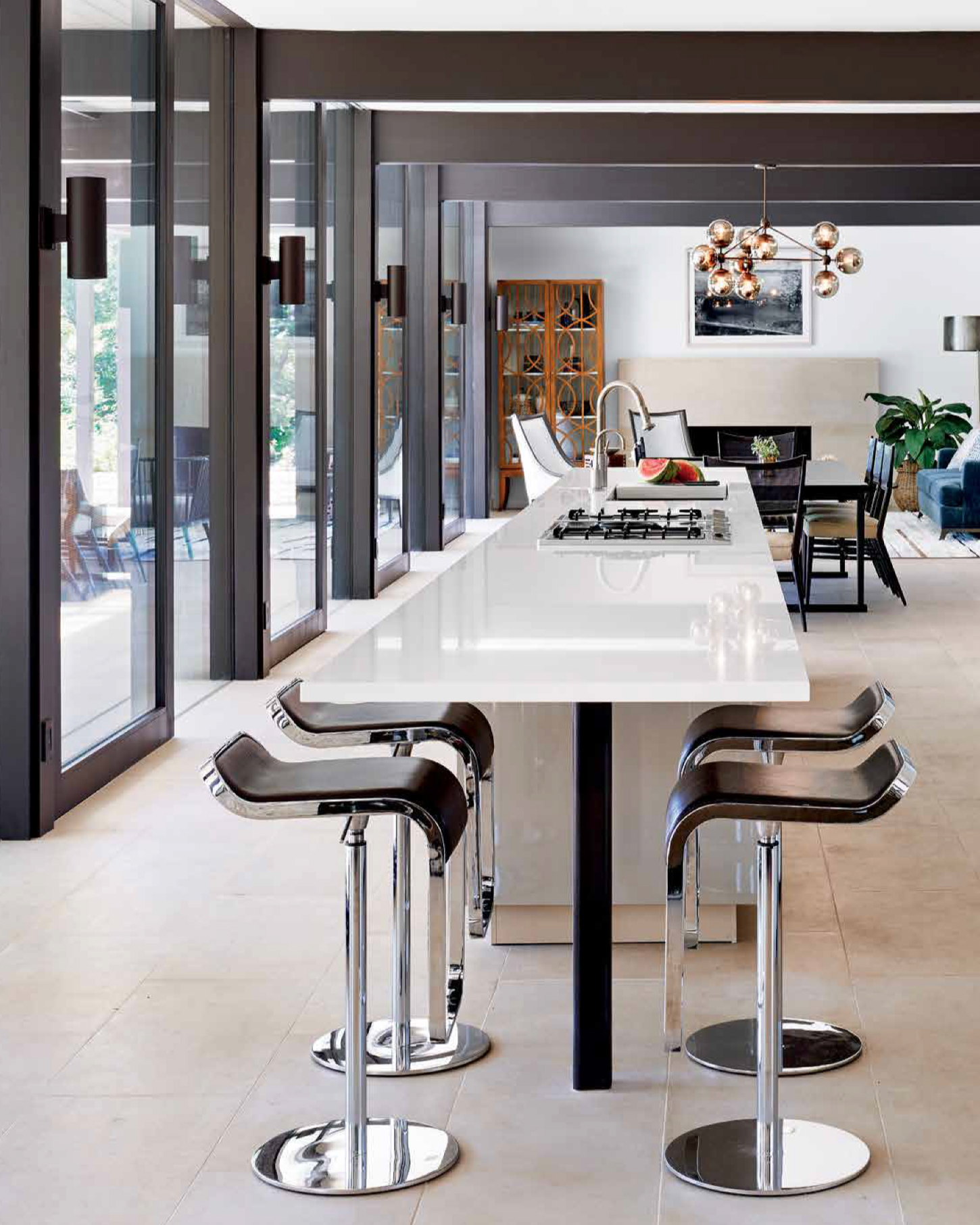 Modern kitchen with white countertops, black barstools, and large sliding glass doors.