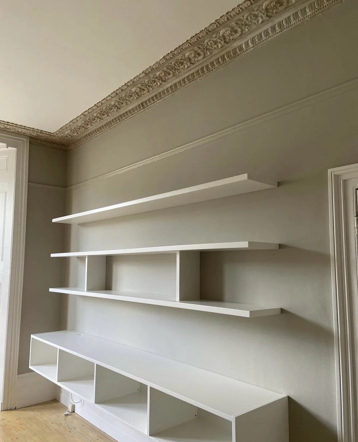 White built-in shelves on beige wall with ornate crown molding in room with hardwood flooring.